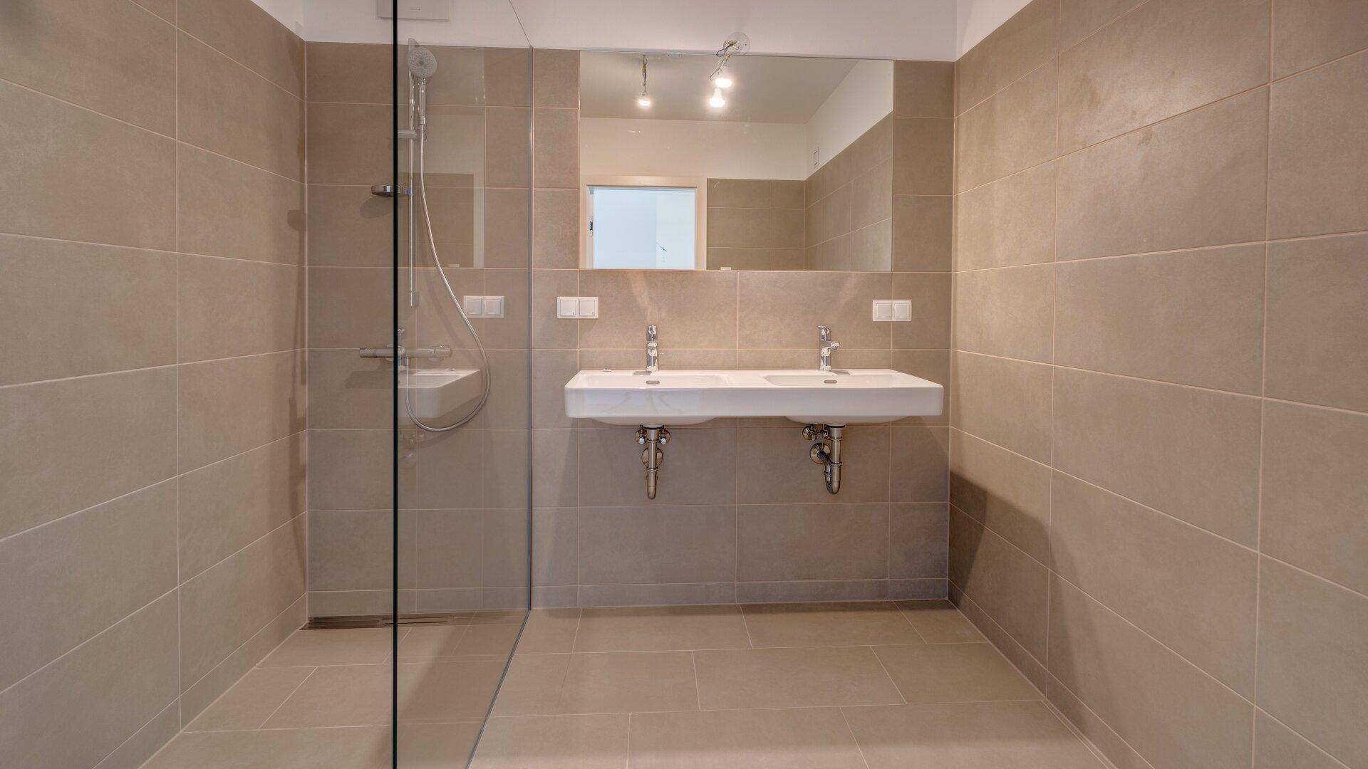 Geräumiges Badezimmer mit großen grauen Fliesen, Doppelwaschbecken und einer begehbaren Dusche.