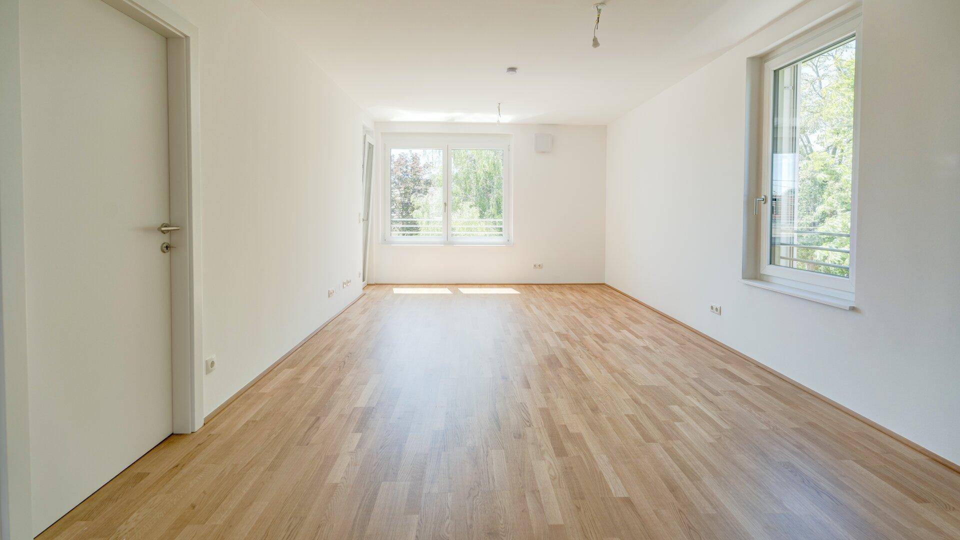 Großes, helles Wohnzimmer mit Holzparkettboden und mehreren Fenstern für viel Tageslicht.