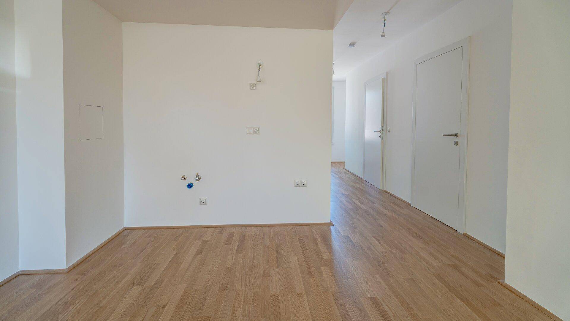 Bereich für eine zukünftige Küche mit allen notwendigen Anschlüssen und hellem Parkettboden.