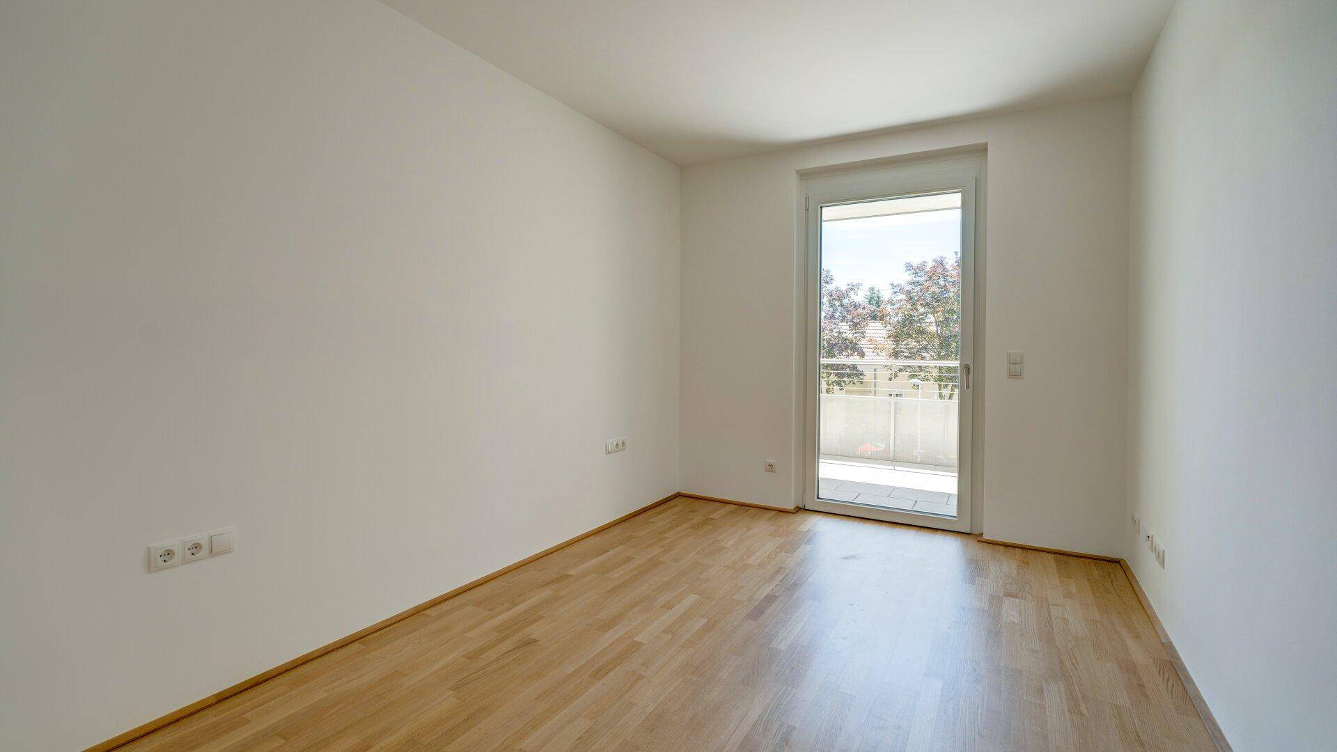 Helles Schlafzimmer mit Holzparkettboden und direktem Zugang zu einem privaten Balkon.