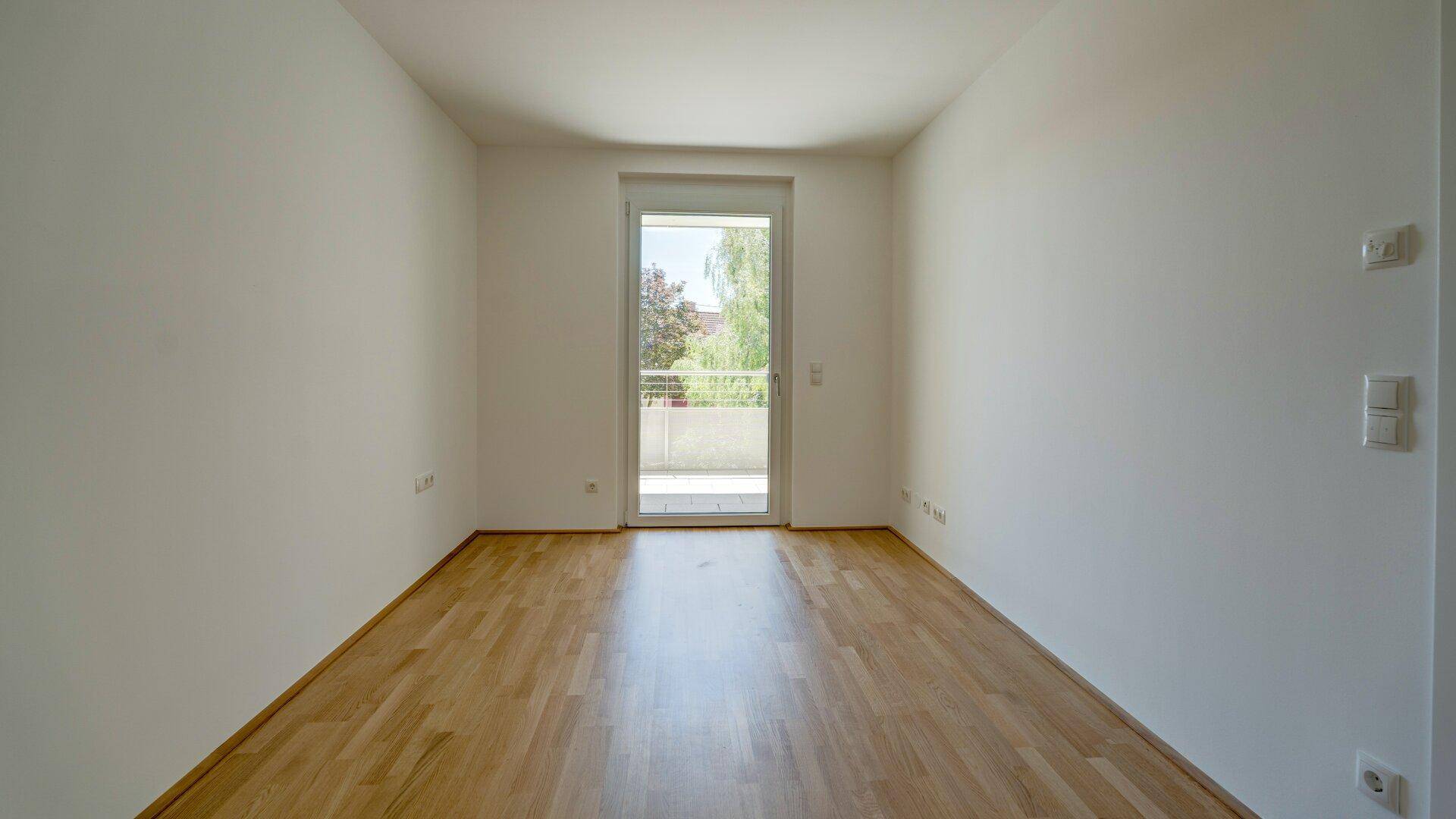 Lichtdurchflutetes Schlafzimmer mit Parkettboden und Balkontür, ideal für sonnige Morgenstunden.