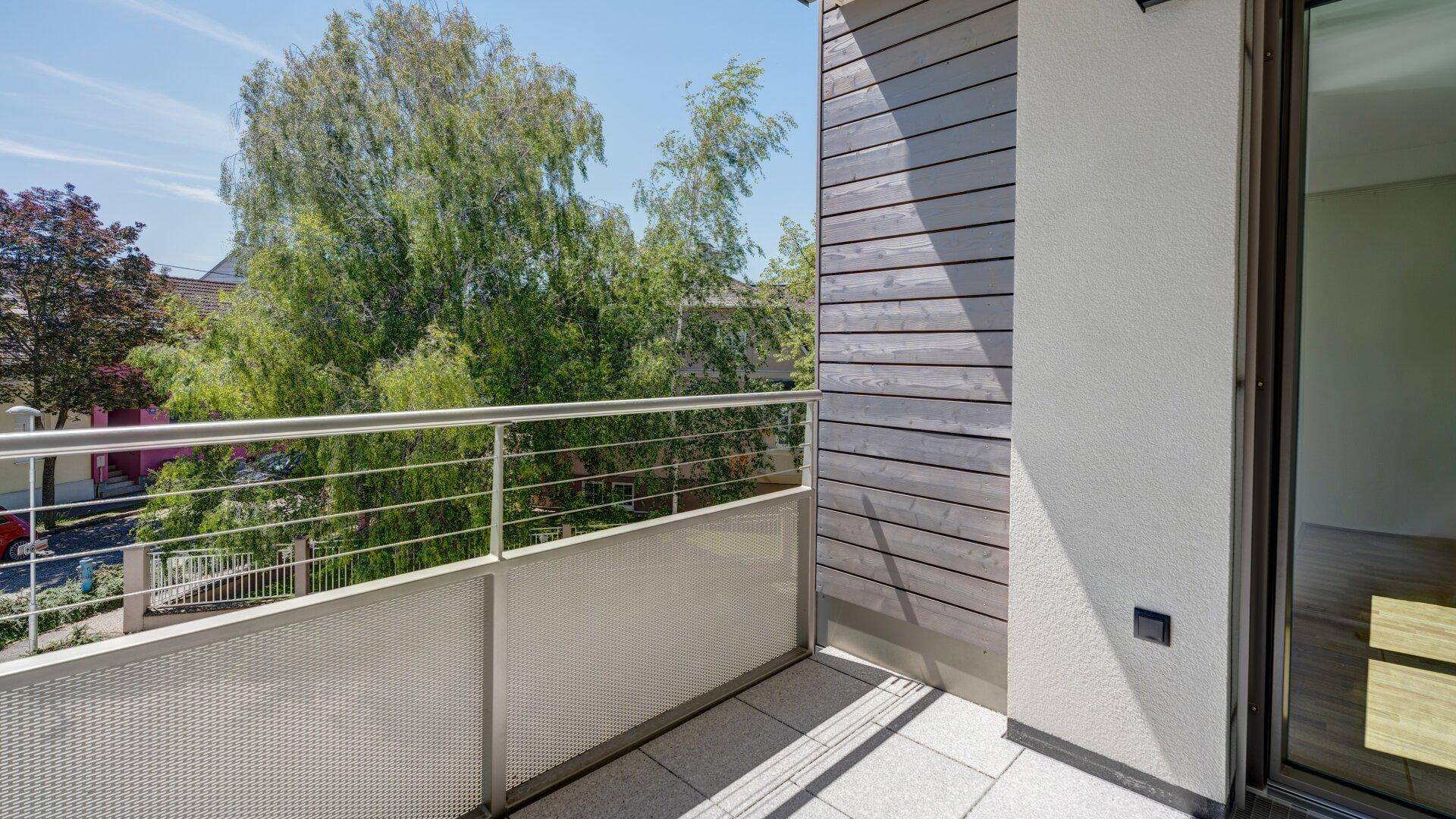 Moderner Balkon mit Fliesenboden, Metallgeländer und Holzverkleidung, umgeben von Bäumen.