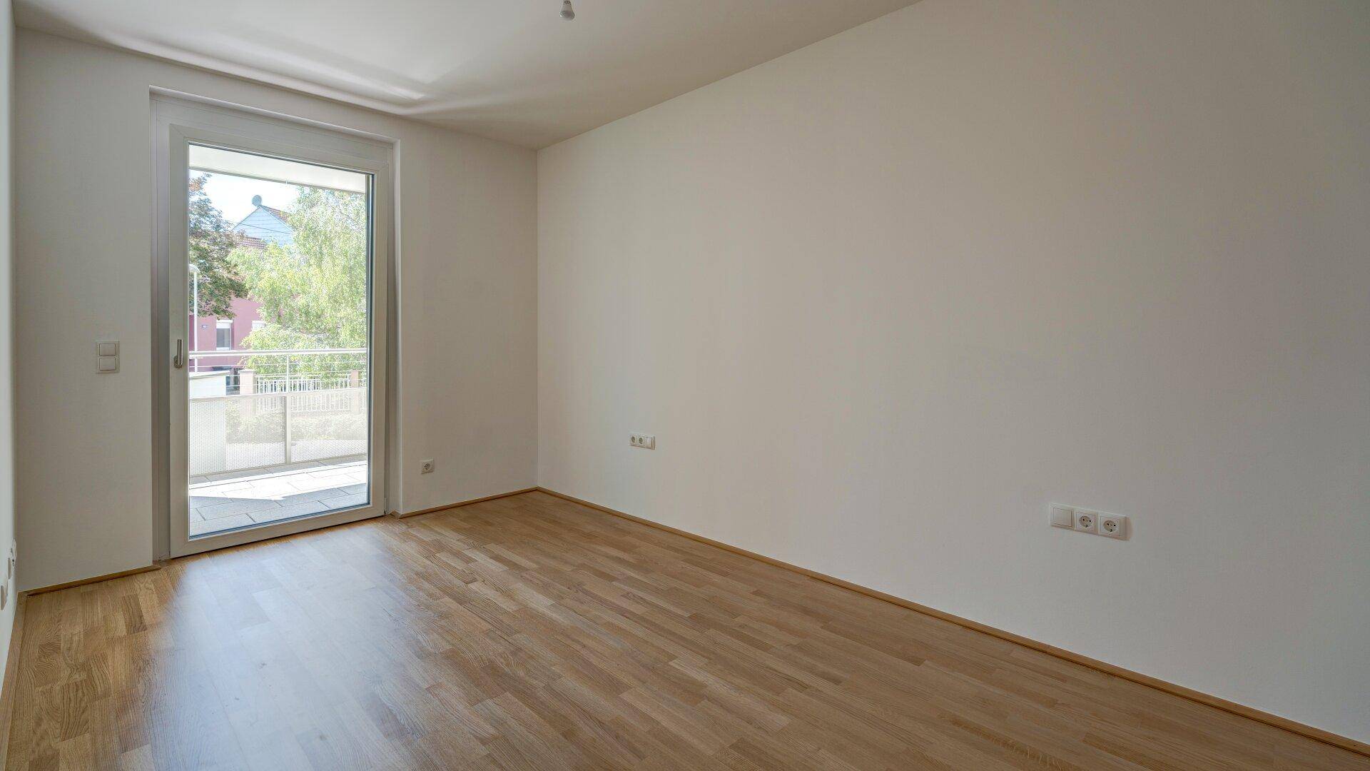 Helles Schlafzimmer mit Parkettboden und direktem Zugang zu einem Balkon, ideal für Morgenkaffee.