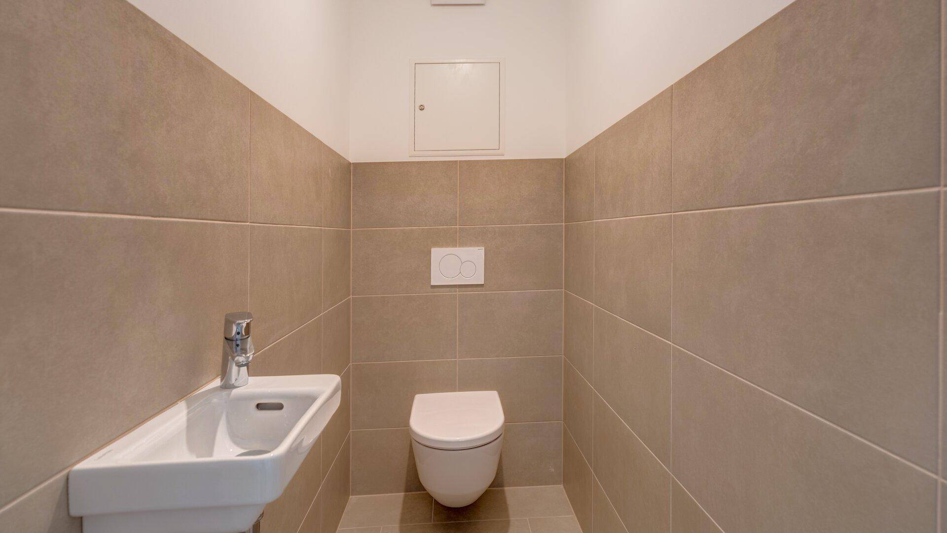 Modernes Gäste-WC mit Wand-WC, kleinem Waschbecken und beigefarbenen Wandfliesen.