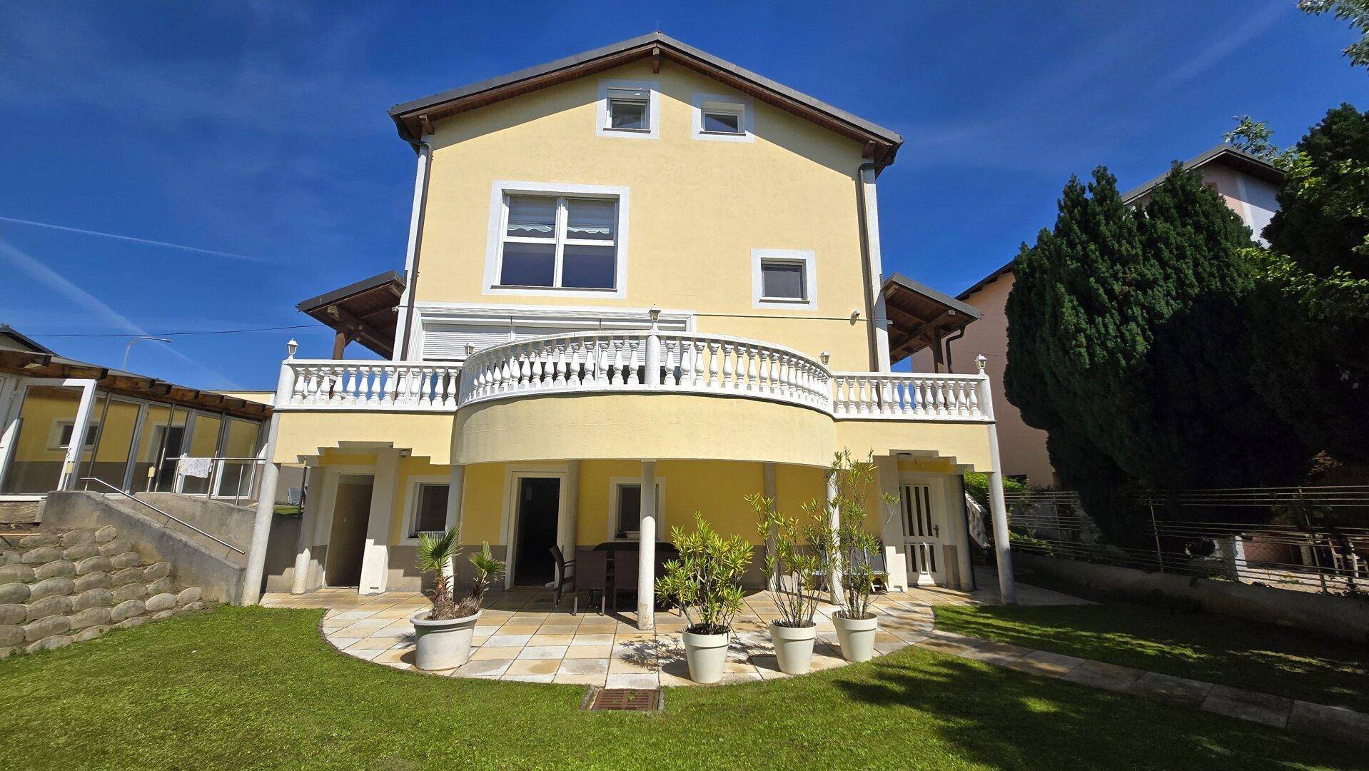 Ansicht des Hauses von hinten mit großem Garten, Terrasse und einem eleganten Balkon.