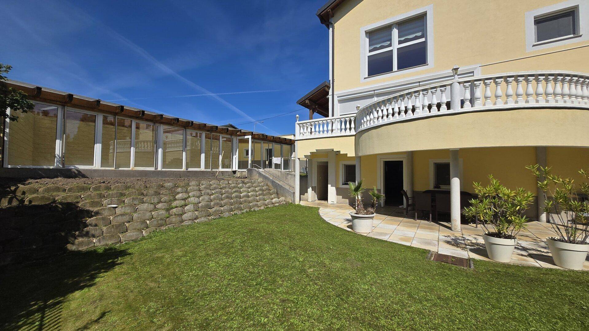 Seitliche Ansicht des Hauses mit weitläufigem Garten, Terrasse und einer Steinmauer.