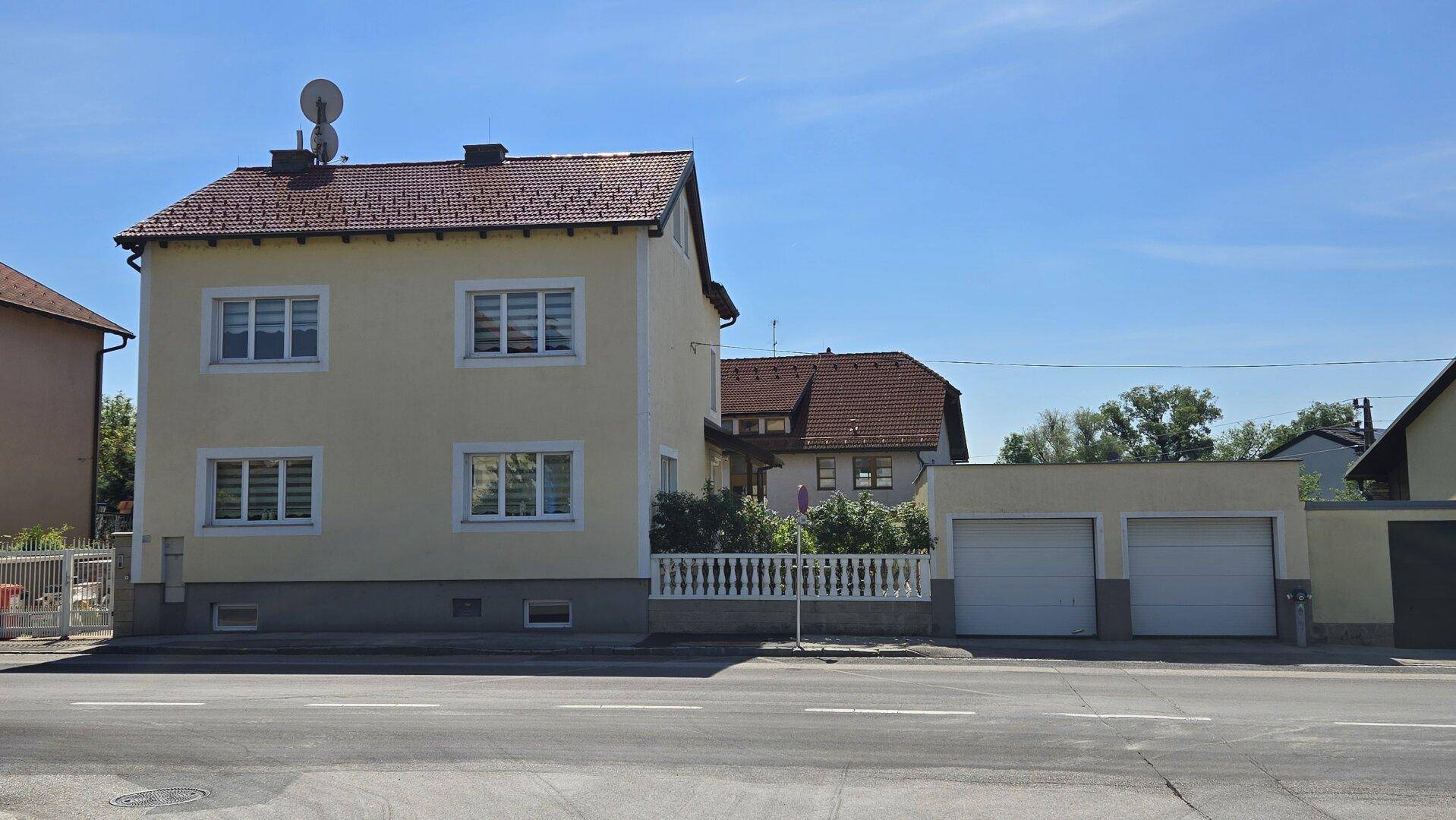 Gelbes Wohnhaus mit rotem Ziegeldach und Doppelgarage, von der Straße aus gesehen.