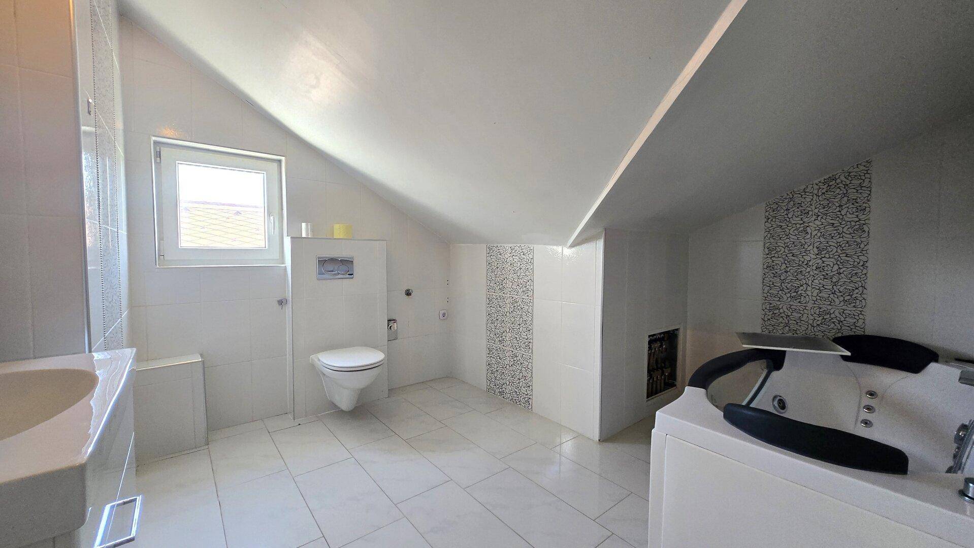 Modernes Badezimmer im Dachgeschoss mit Whirlpool, WC und weißen Fliesen.