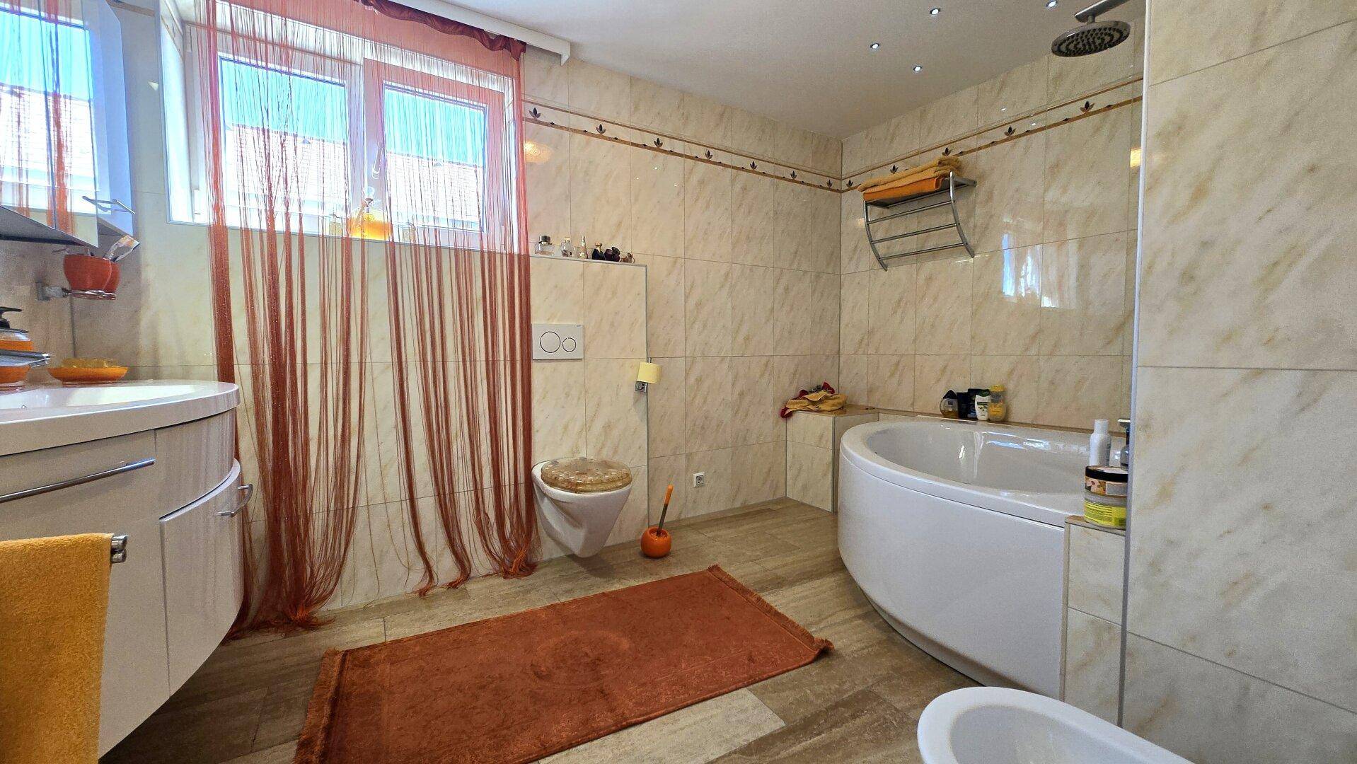 Geräumiges Badezimmer mit Eckbadewanne, Dusche, WC und Fliesen in Marmoroptik.