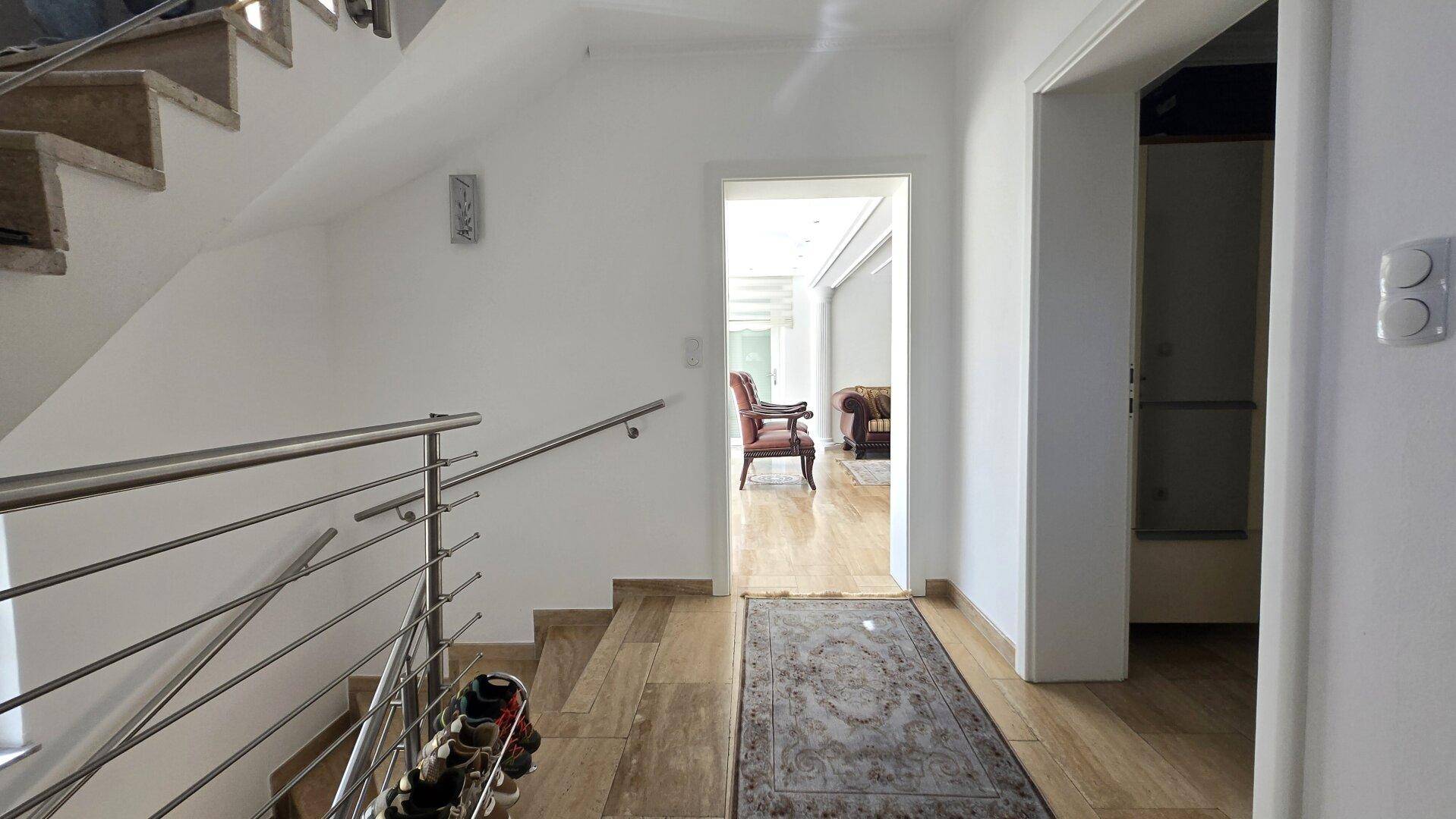 Heller Flur mit Holztreppe, modernem Geländer und Zugang zu weiteren Räumen.
