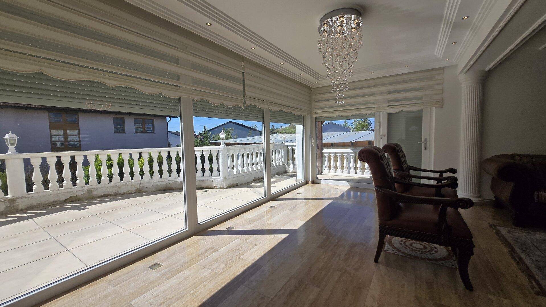 Geräumiges Wohnzimmer mit großen Fenstern, Zugang zum Balkon und elegantem Kronleuchter.