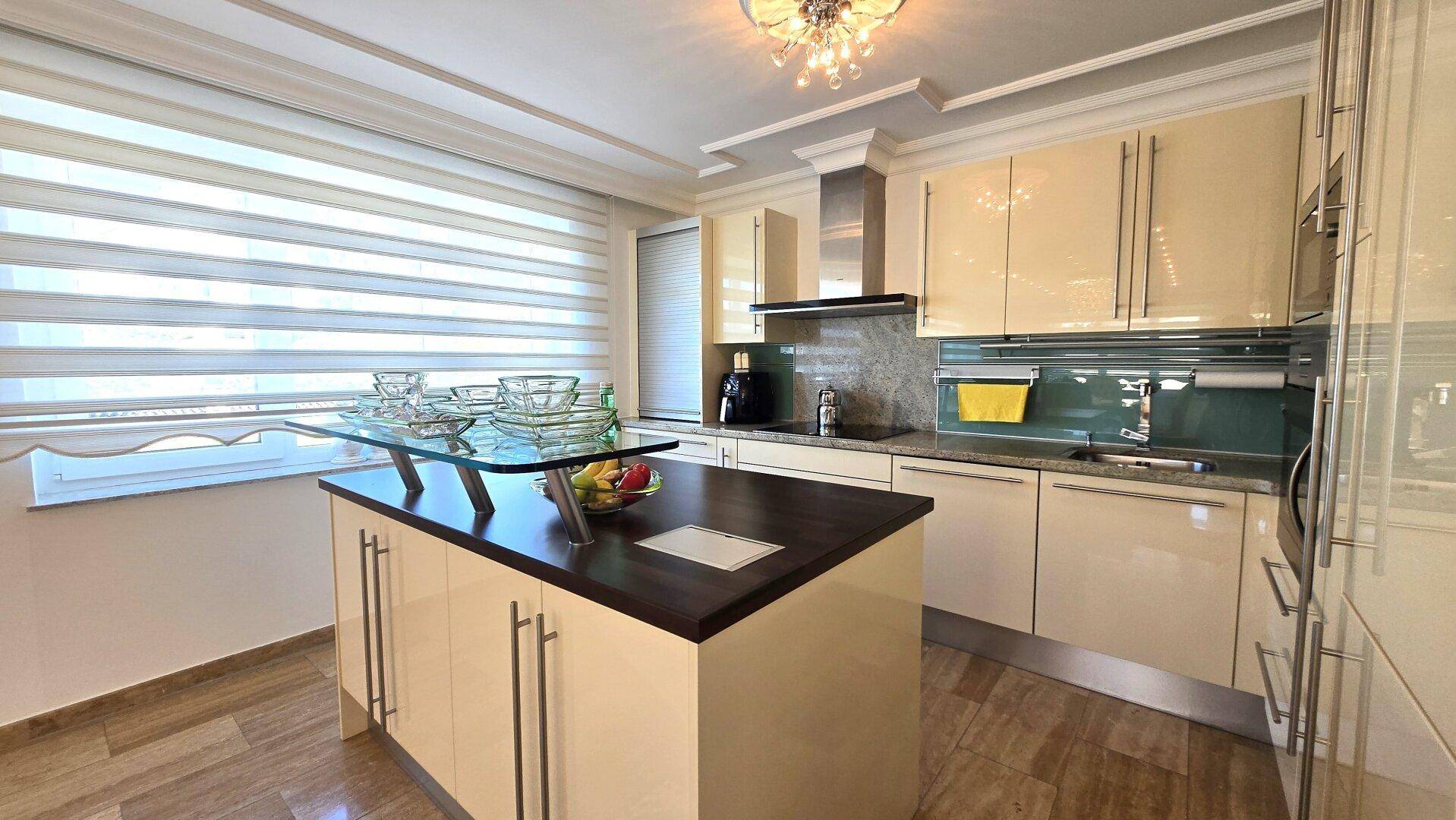 Moderne Küche mit beigen Hochglanzfronten, Kücheninsel und integrierten Geräten.