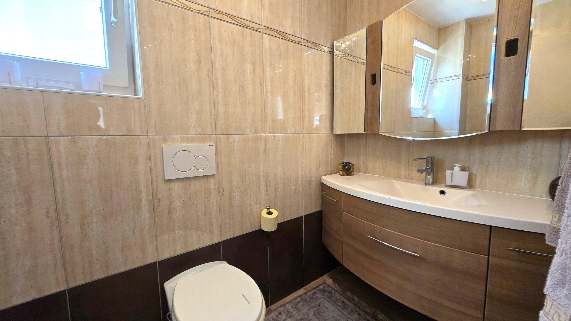 Kleines Gäste-WC mit Wand-WC, Einzelwaschbecken und Fliesen in Beige- und Brauntönen.