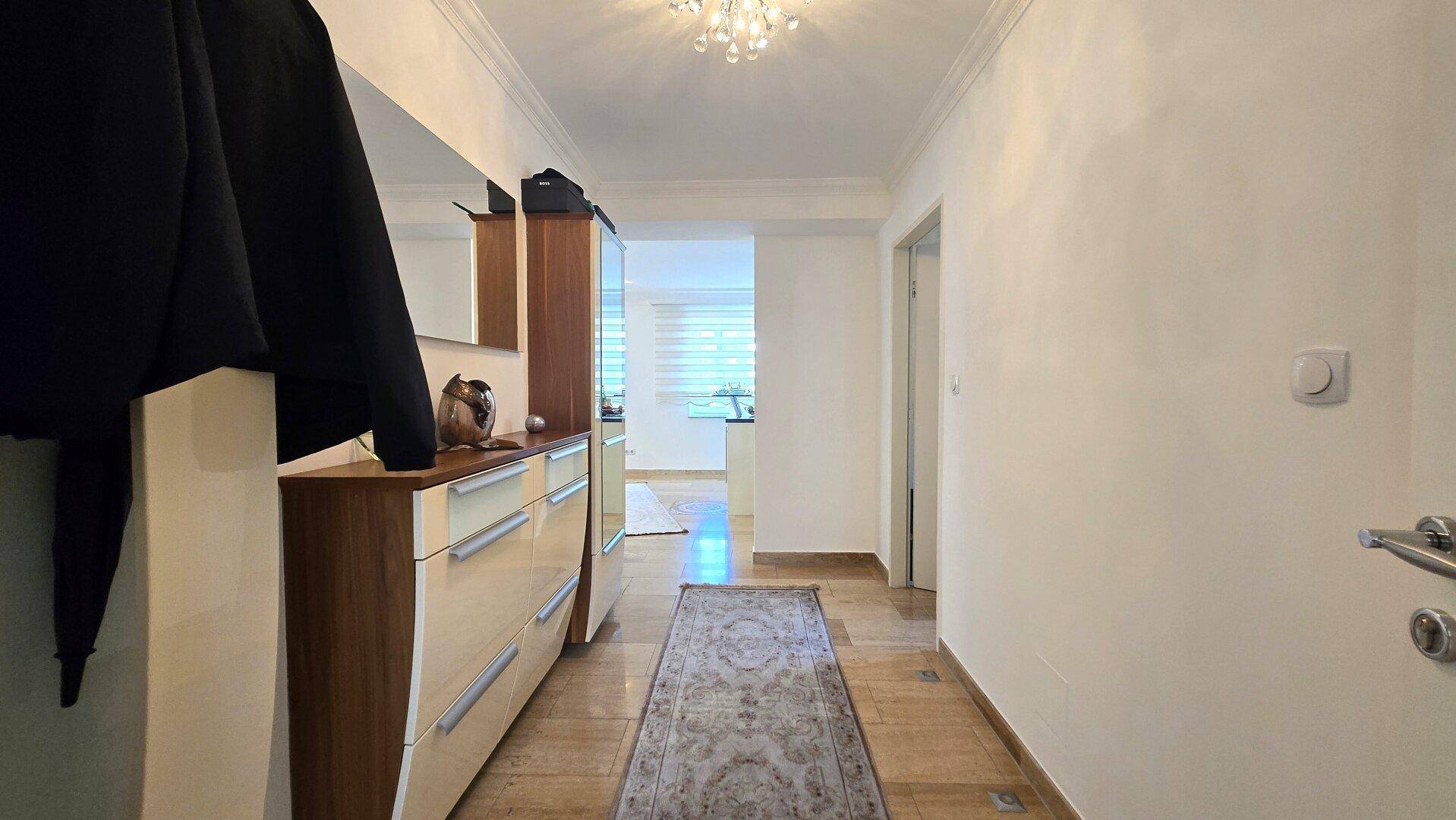 Eingangsbereich mit Garderobe, Spiegel und einem Teppich auf Fliesenboden.