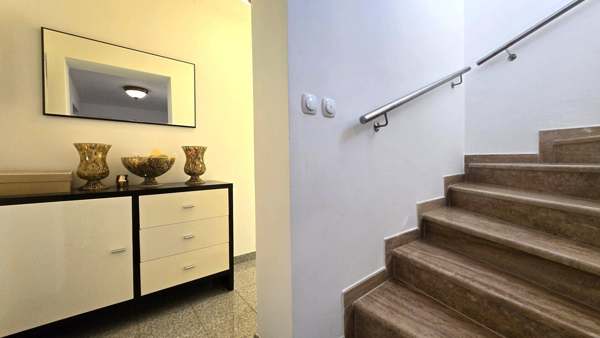 Eingangsbereich mit eleganter Konsole, Spiegel und einer Treppe mit modernem Metallgeländer.