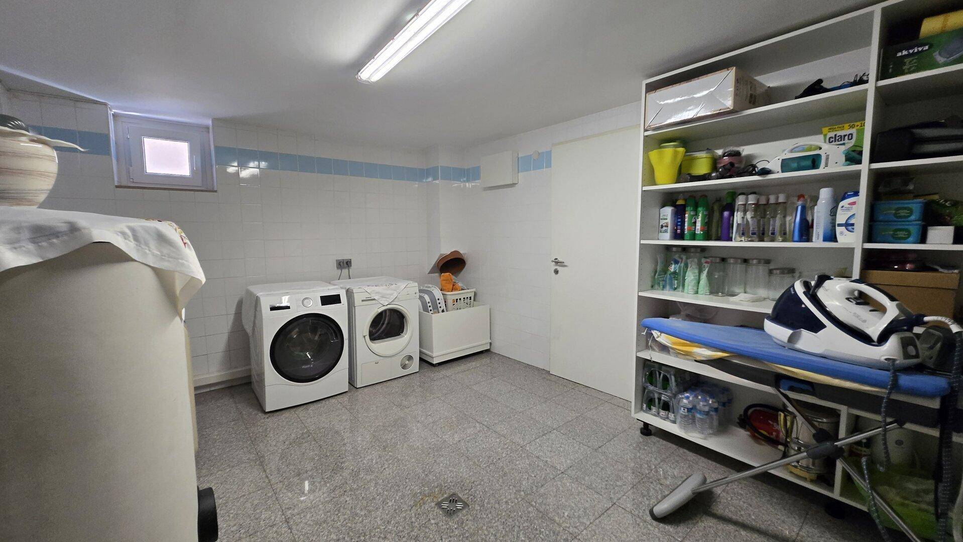 Praktischer Hauswirtschaftsraum mit Waschmaschine, Trockner, Regalen und kleinem Fenster.