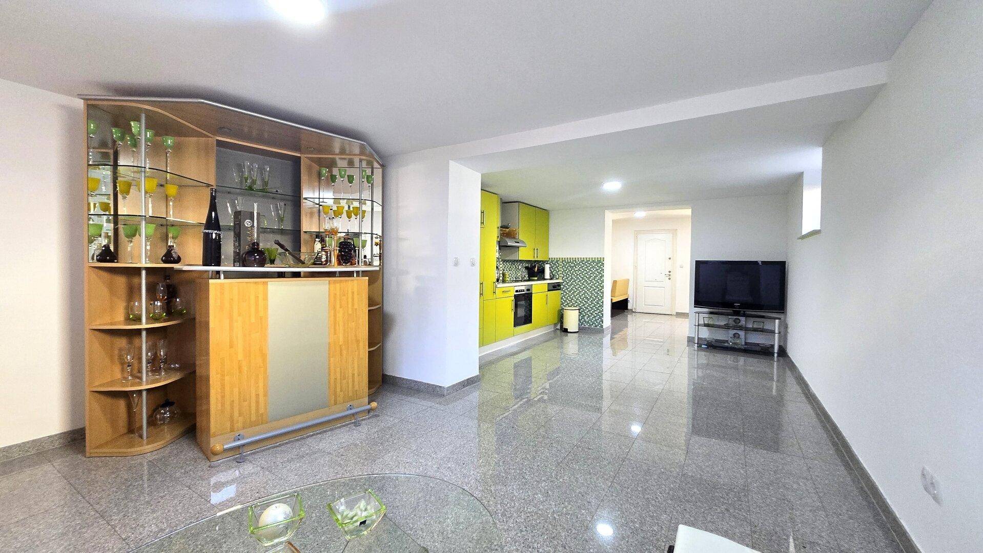 Offener Wohnbereich mit Bar, Fernseher und integrierter Küche, ideal für Unterhaltung und Geselligkeit.