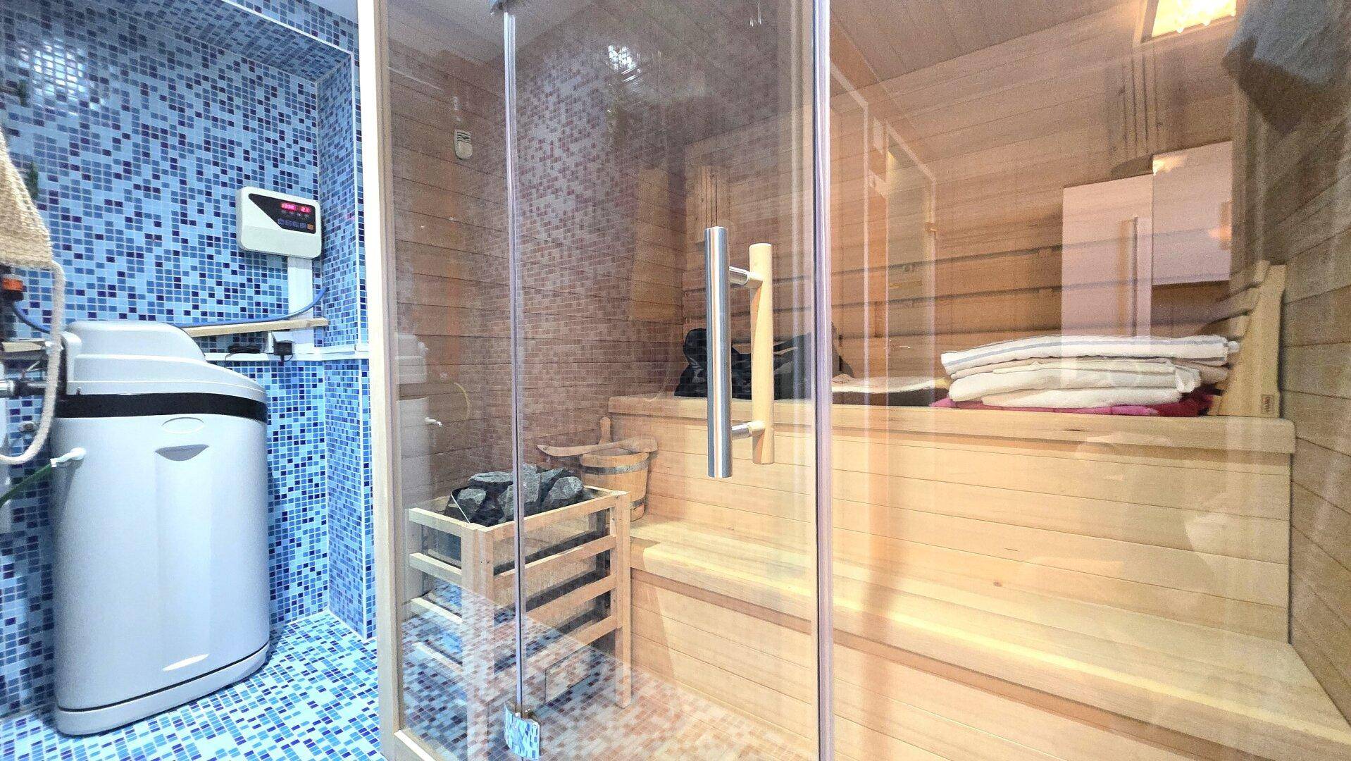 Badezimmer mit blauen Mosaikfliesen, einer Duschkabine und einer integrierten Holzsauna.