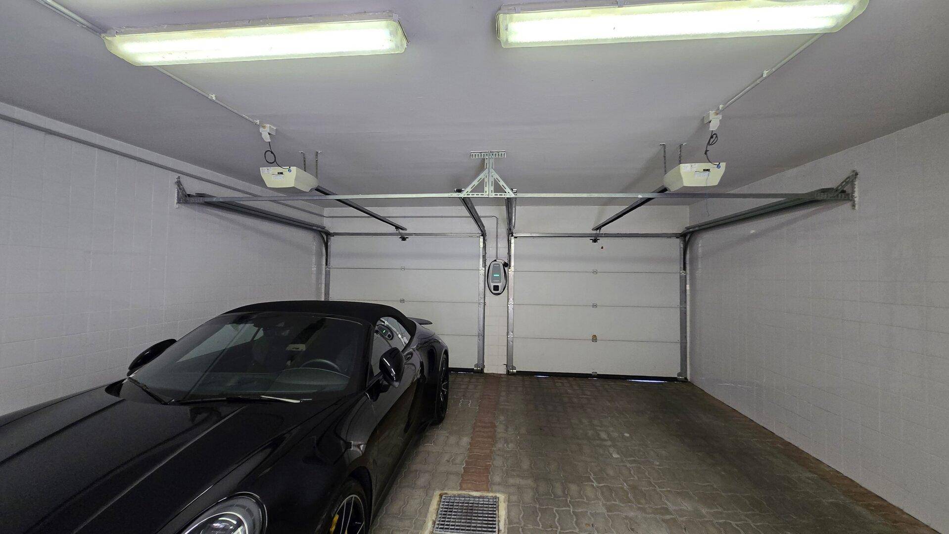 Geräumige Garage mit zwei Toren, einem Sportwagen und einer Ladestation für Elektrofahrzeuge.