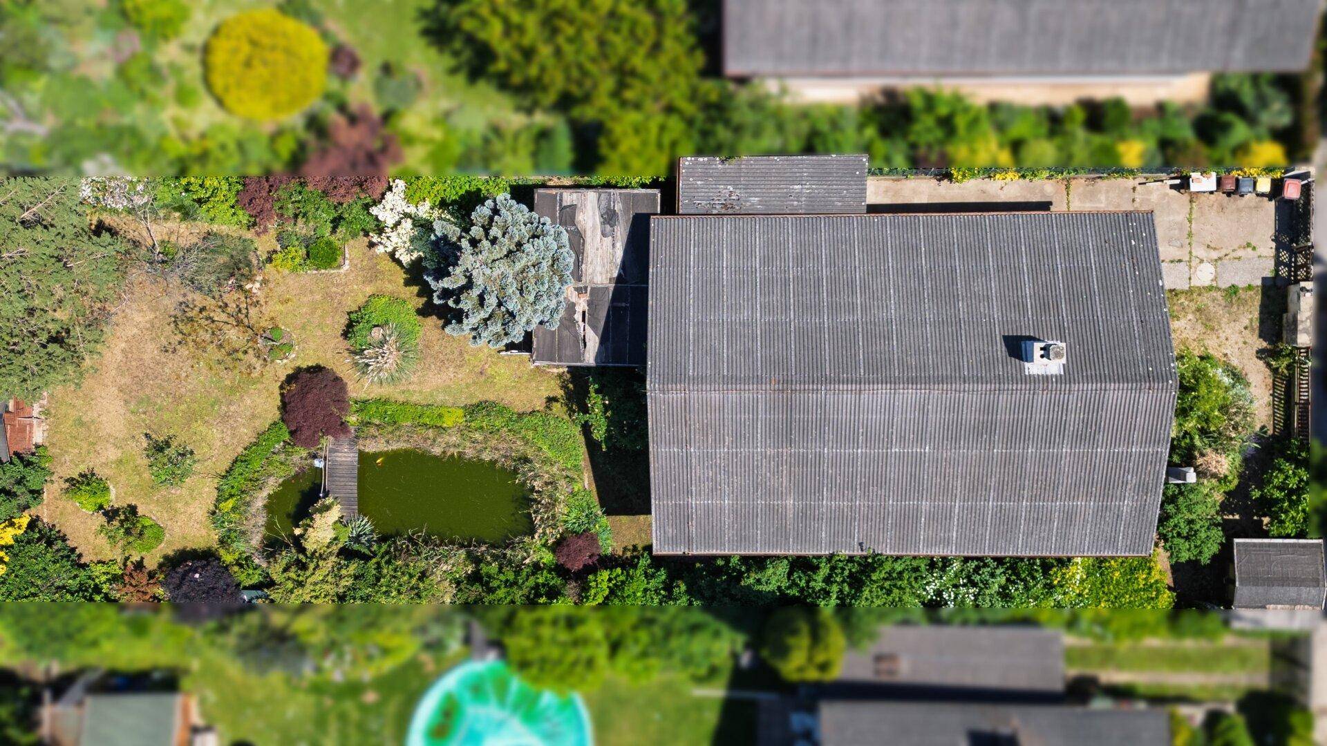 Luftaufnahme des Grundstücks mit Wohnhaus, Garten, Teich und umliegender Vegetation.