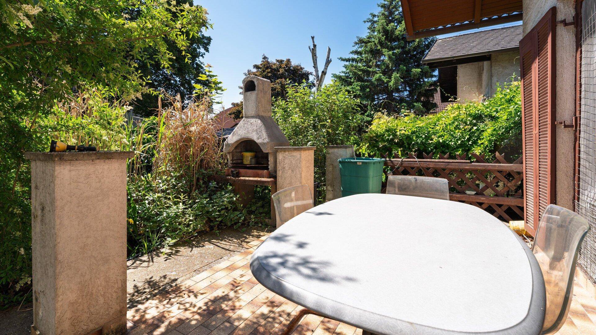 Gemütliche Terrasse mit Esstisch und gemauertem Grill, ideal für Mahlzeiten im Freien.