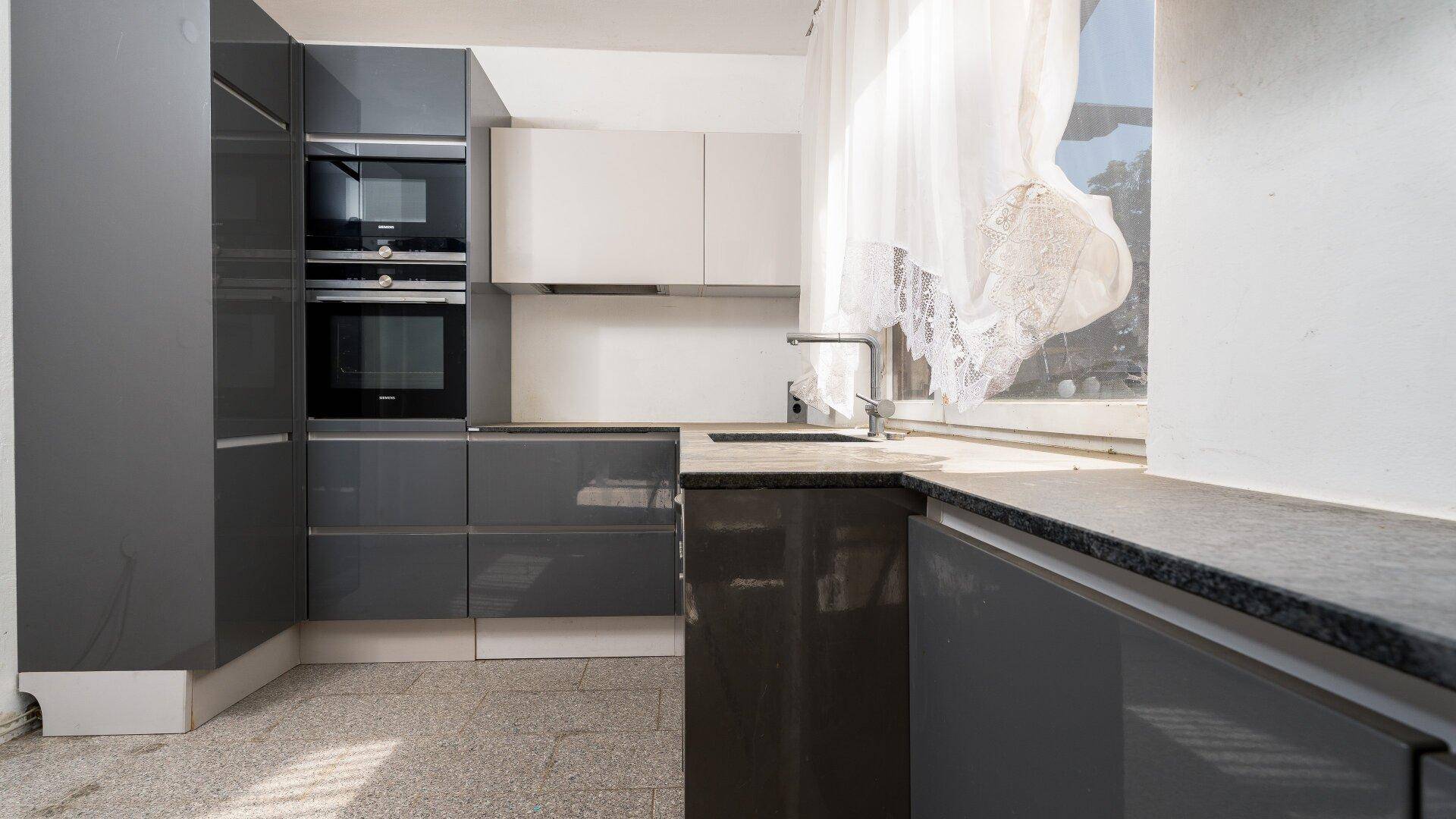Moderne Einbauküche mit grauen Schränken, dunkler Arbeitsplatte und integrierten Geräten.