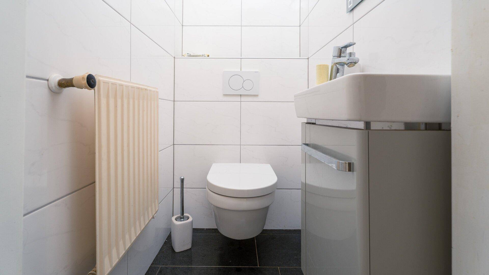 Modernes Gäste-WC mit weißen Fliesen, wandhängendem WC und kleinem Waschbecken.