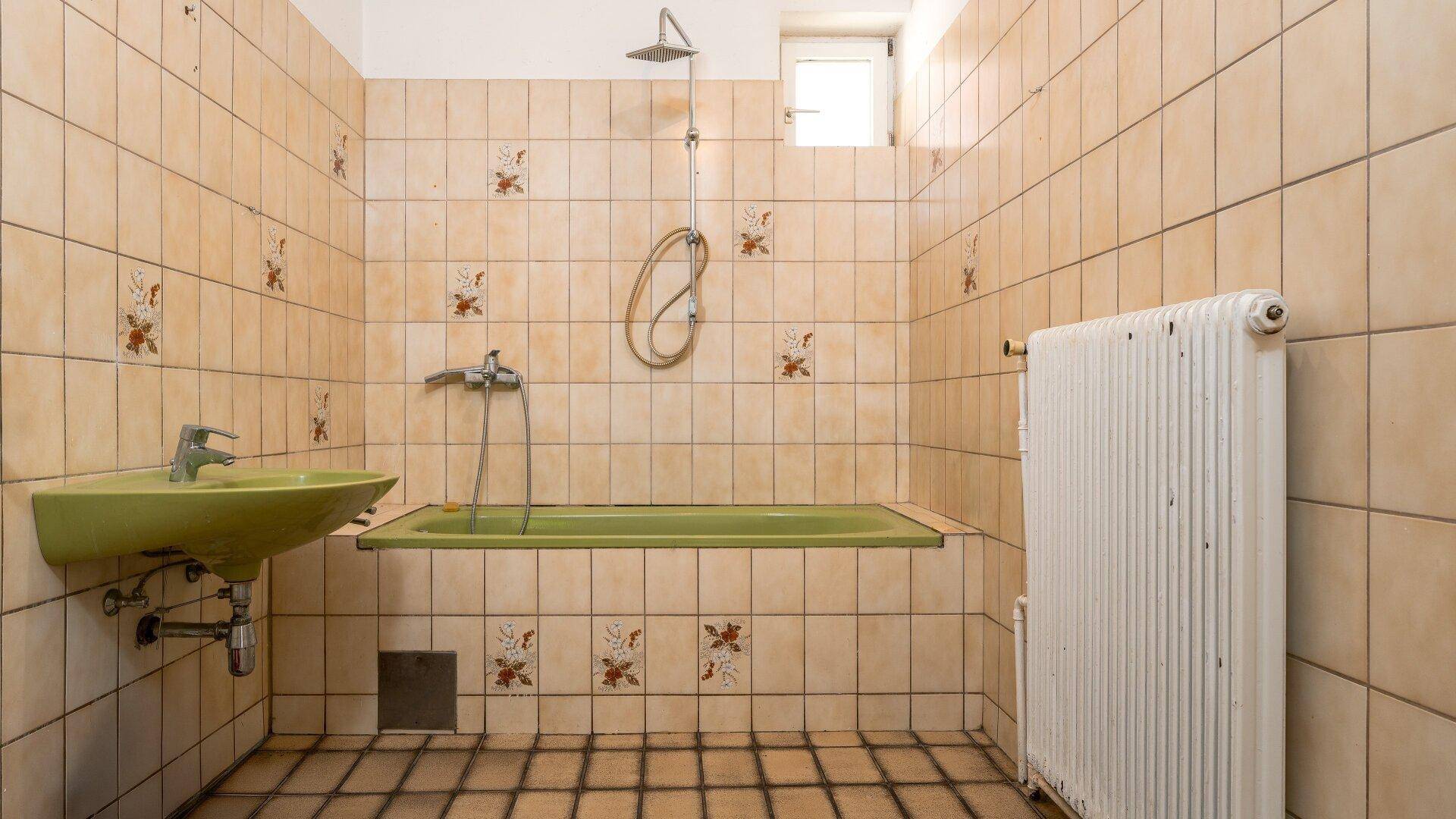 Badezimmer im Stil der 80er Jahre mit grüner Badewanne, Waschbecken und gemusterten Fliesen.