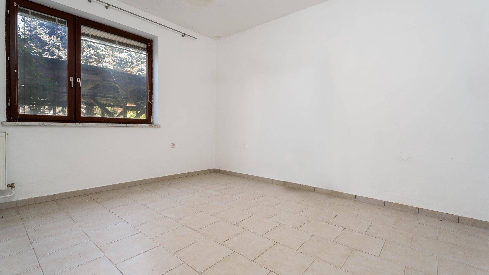 Geräumiges Zimmer mit hellen Fliesen und großem Fenster, das den Raum erhellt.