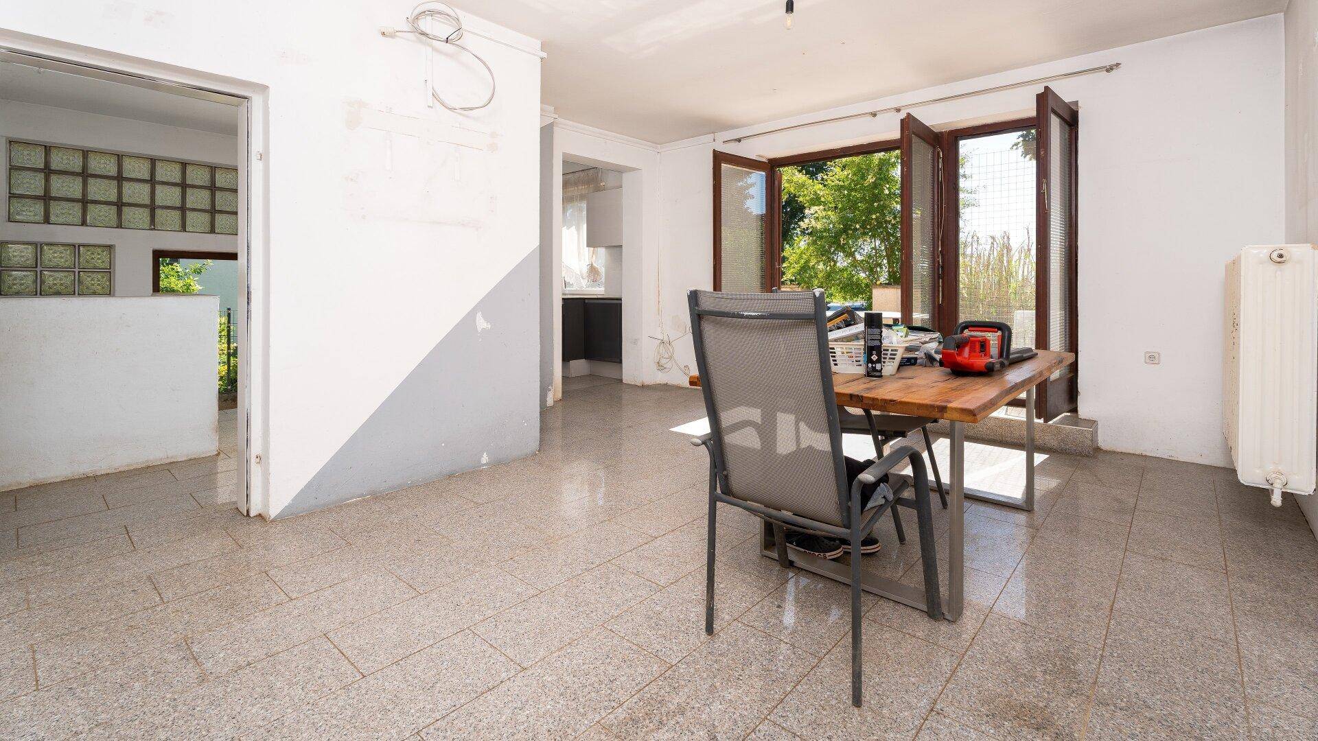 Geräumiger Wohnbereich mit Terrassenzugang und Blick auf den Garten, teilweise renovierungsbedürftig.