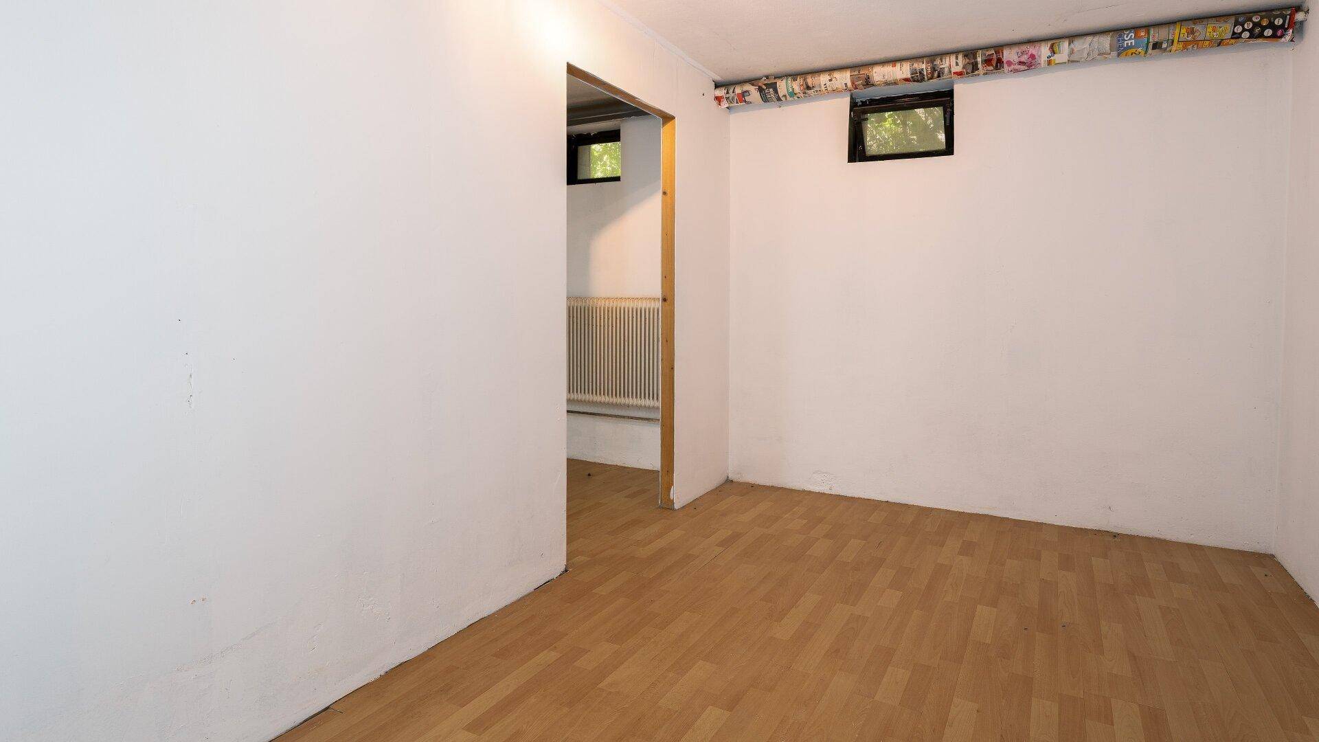 Kellerraum mit Laminatboden und kleinen Fenstern, der als zusätzlicher Wohnraum genutzt werden könnte.