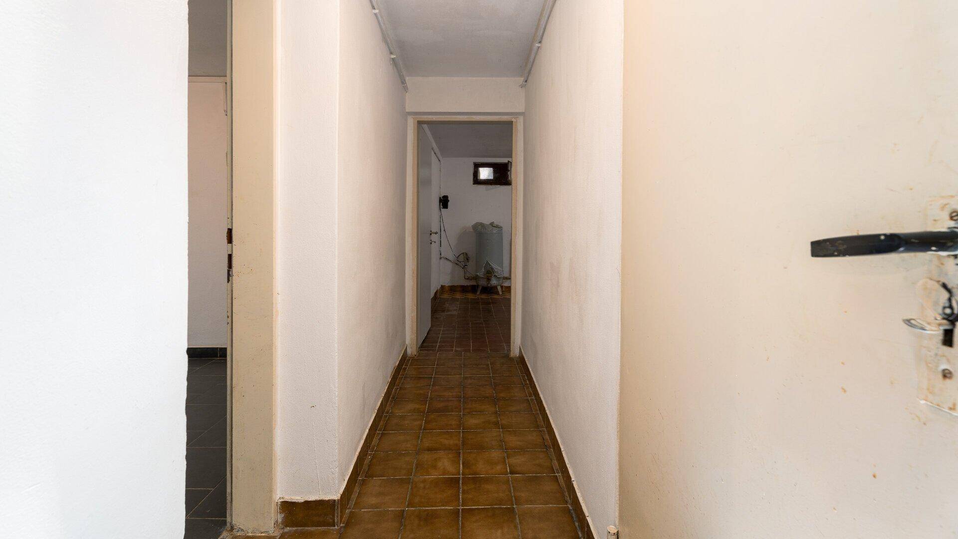Langer Flur mit braunen Fliesen, der verschiedene Räume im Untergeschoss verbindet.