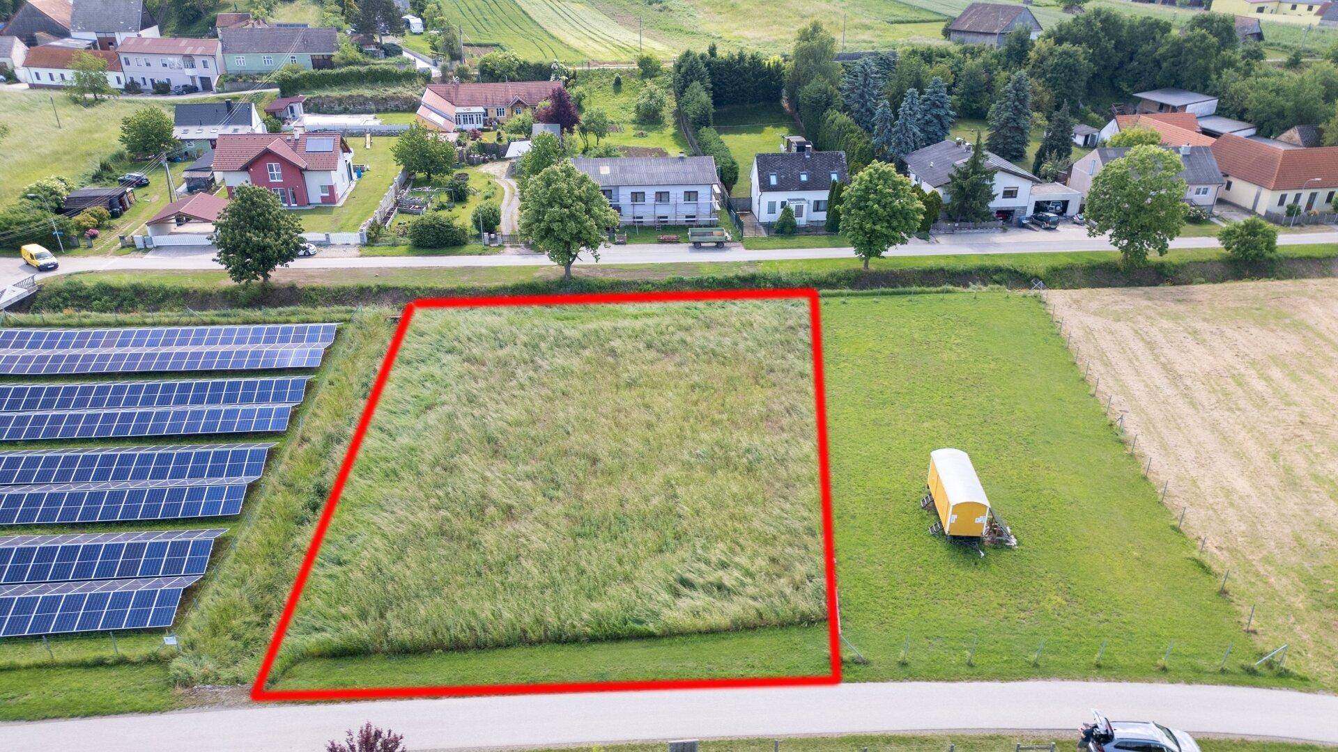 Übersicht aus der Vogelperspektive eines grünen Baugrundstücks neben einer Solaranlage und Wohnhäusern.