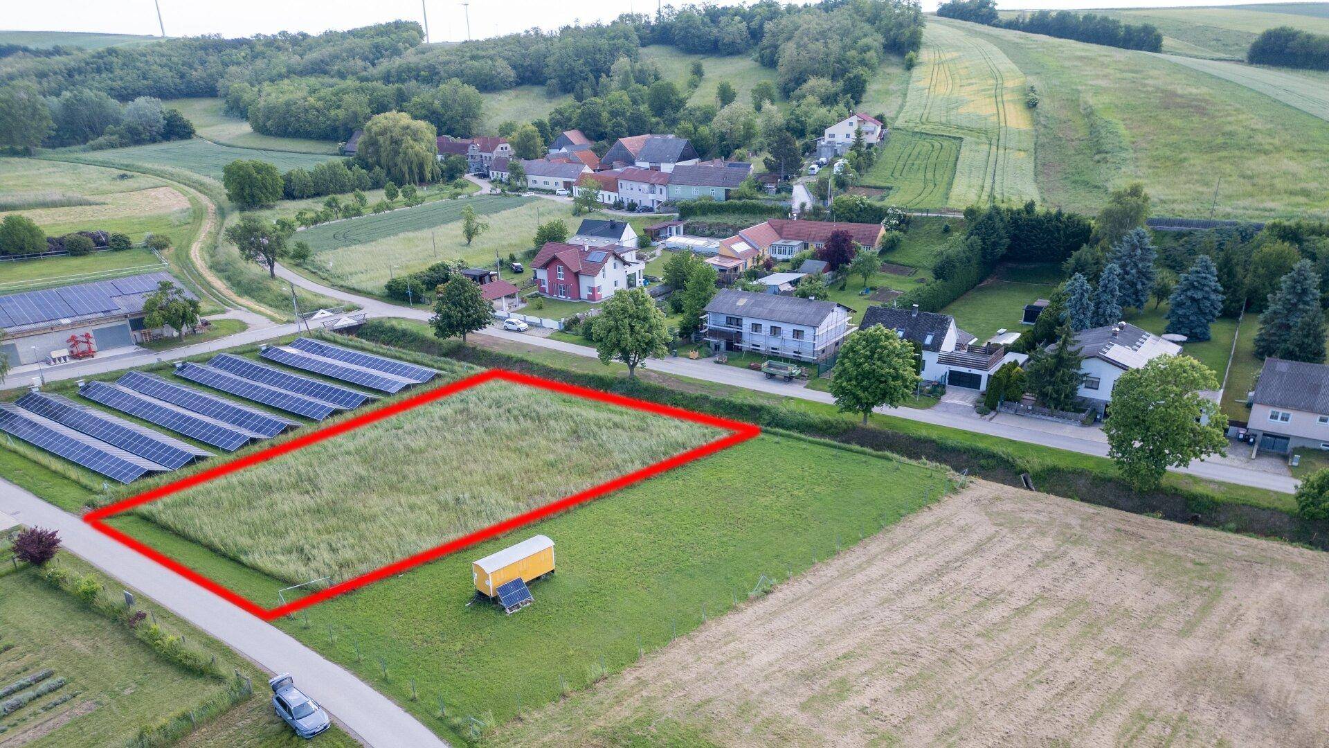 Luftbild des Baugrundstücks mit Solaranlage, umgeben von ländlicher Bebauung und grünen Hügeln.