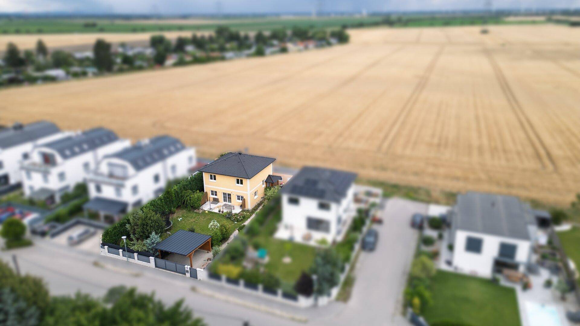 Luftaufnahme des Wohnhauses mit Garten, Carport und angrenzenden Feldern.