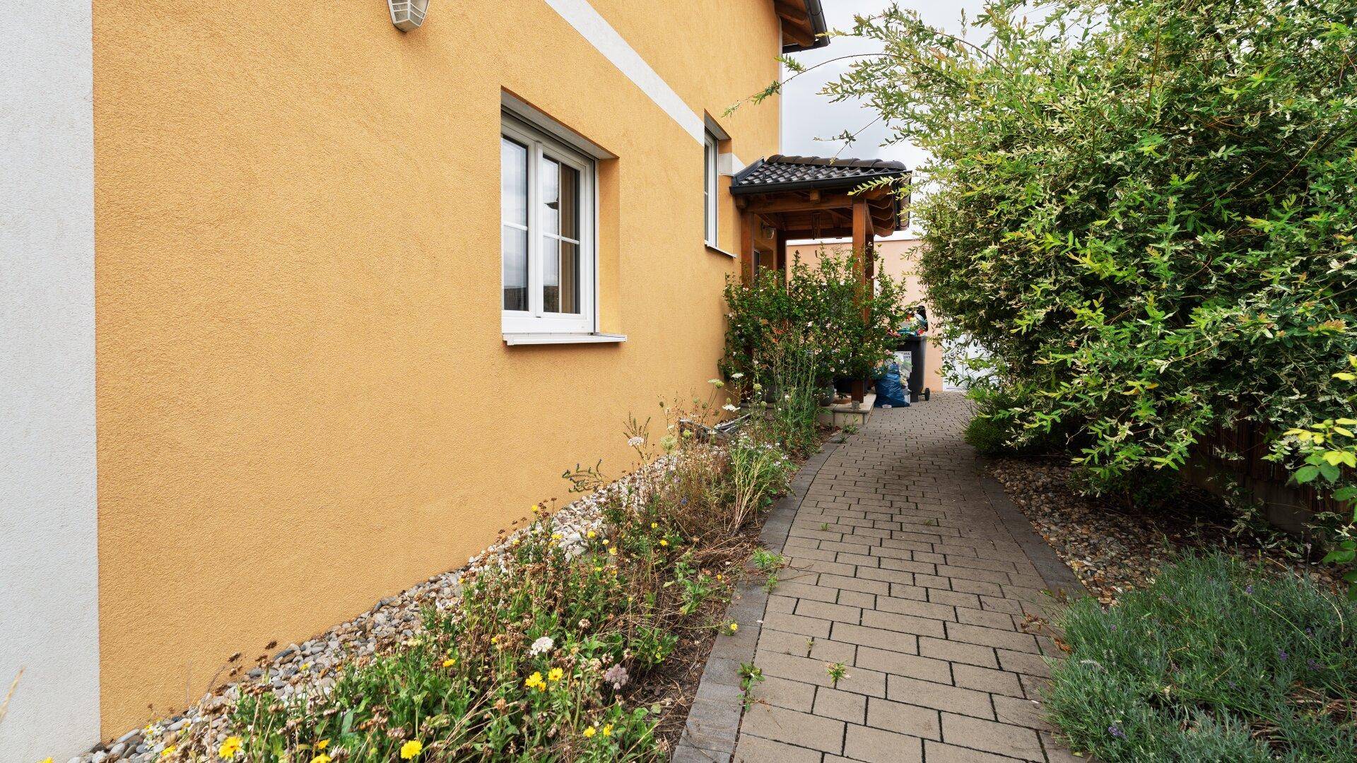 Seitenansicht des Hauses mit gelber Fassade und einem gepflasterten Weg zum Eingang.