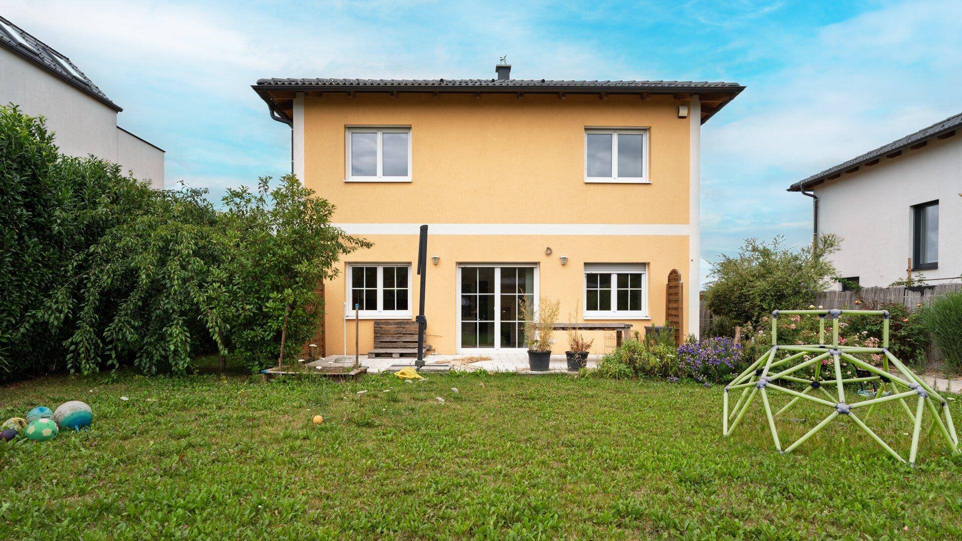 Rückansicht des Hauses mit Garten, Terrasse und Spielgeräten für Kinder.