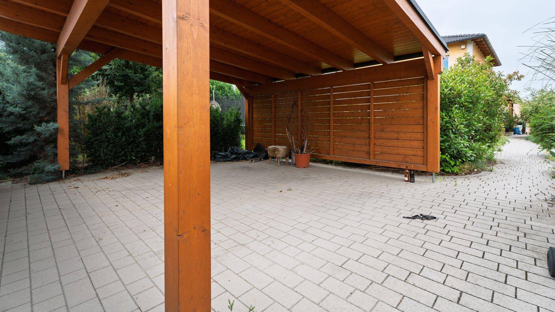 Geräumiger Carport mit Holzkonstruktion und gepflastertem Stellplatz.