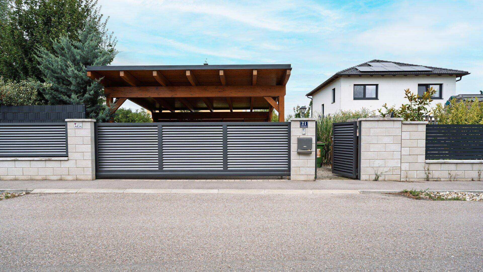 Moderne Einfahrt mit Schiebetor, Zaun und Carport im Hintergrund.