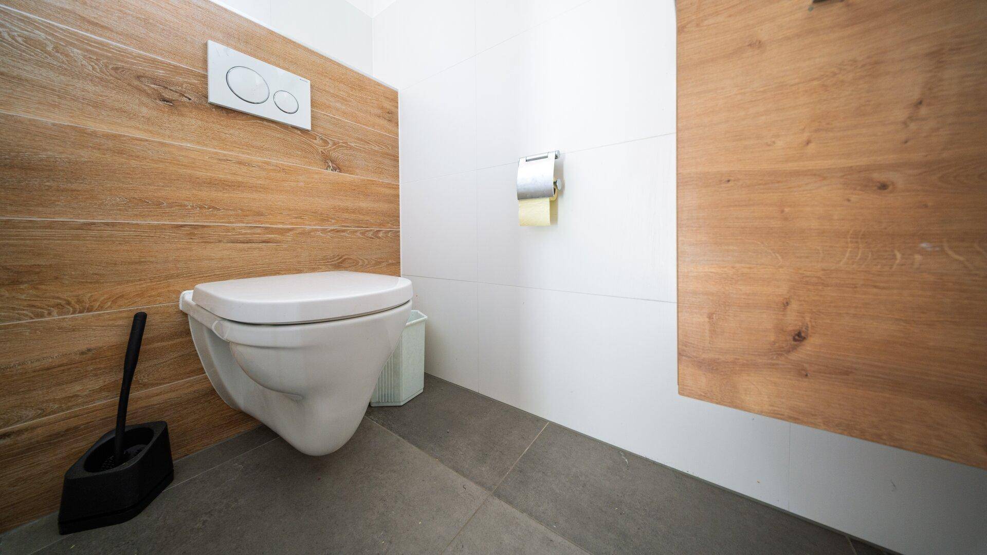 Modernes Gäste-WC mit wandhängender Toilette und Holzakzenten an der Wand.
