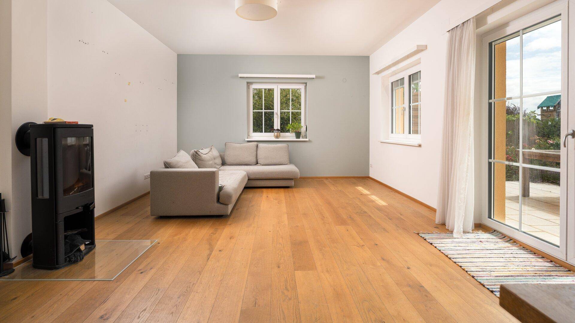 Geräumiges Wohnzimmer mit Holzboden, Kaminofen und Zugang zur Terrasse.
