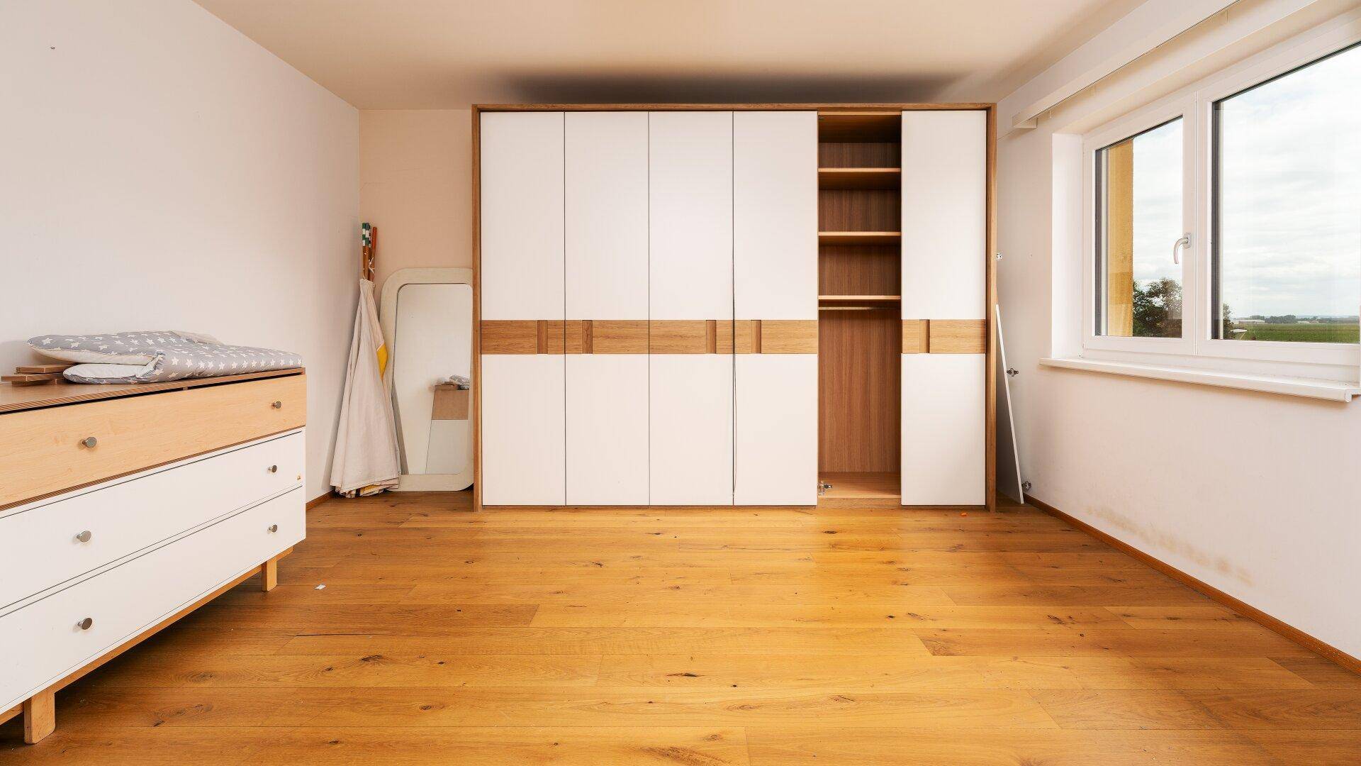 Schlafzimmer mit Holzboden, großem Kleiderschrank und viel Tageslicht.
