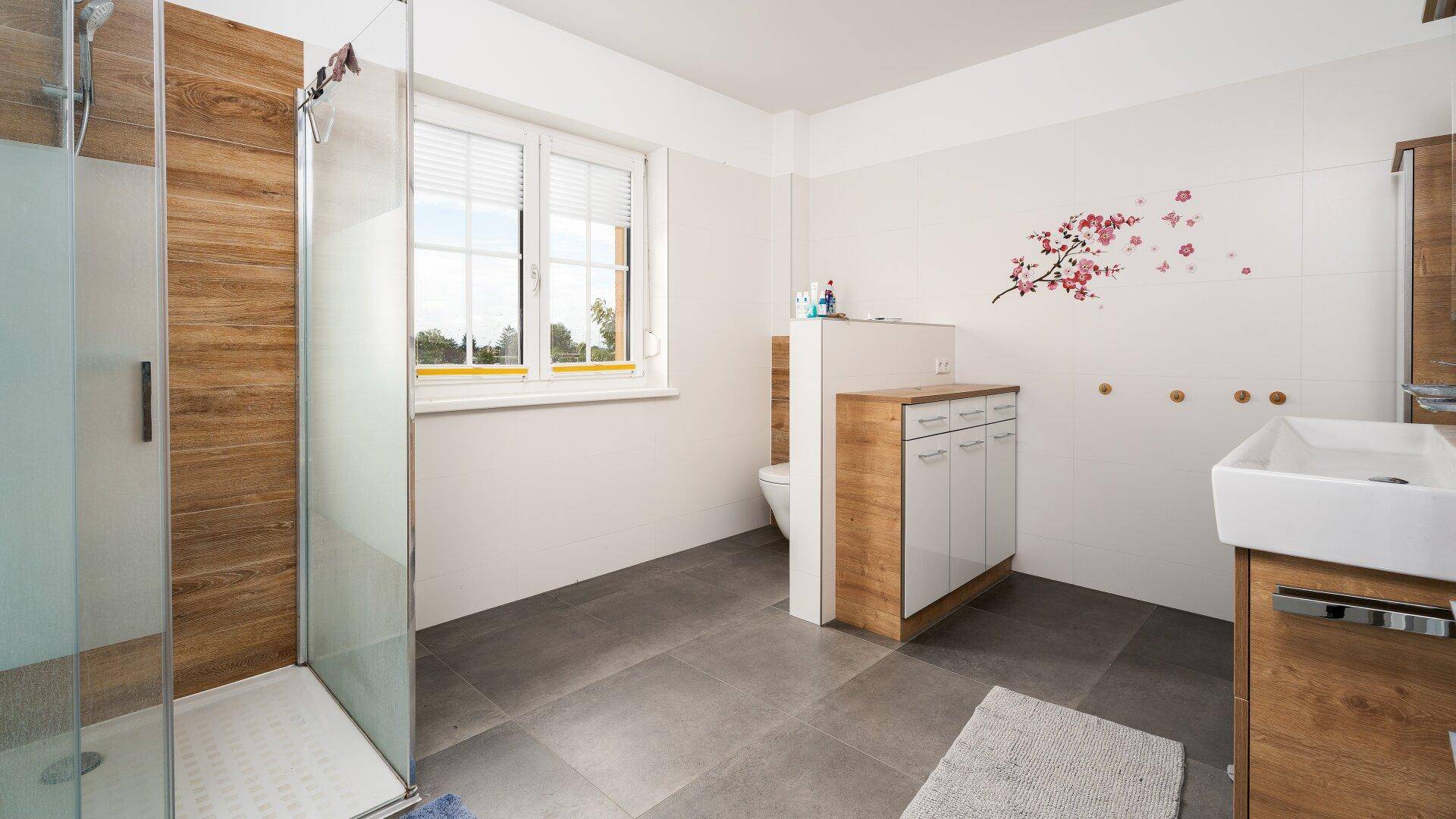 Modernes Badezimmer mit ebenerdiger Dusche, WC und Fenster.
