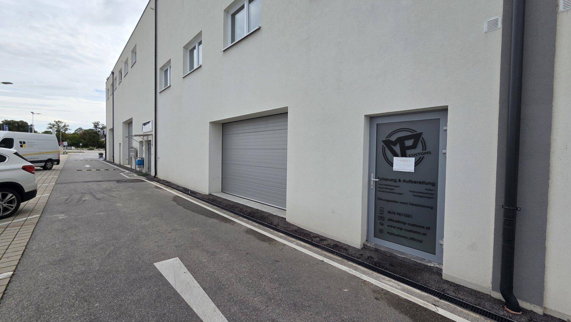 Seitenansicht eines weißen Geschäftsgebäudes mit Garagentor und Eingangstür.