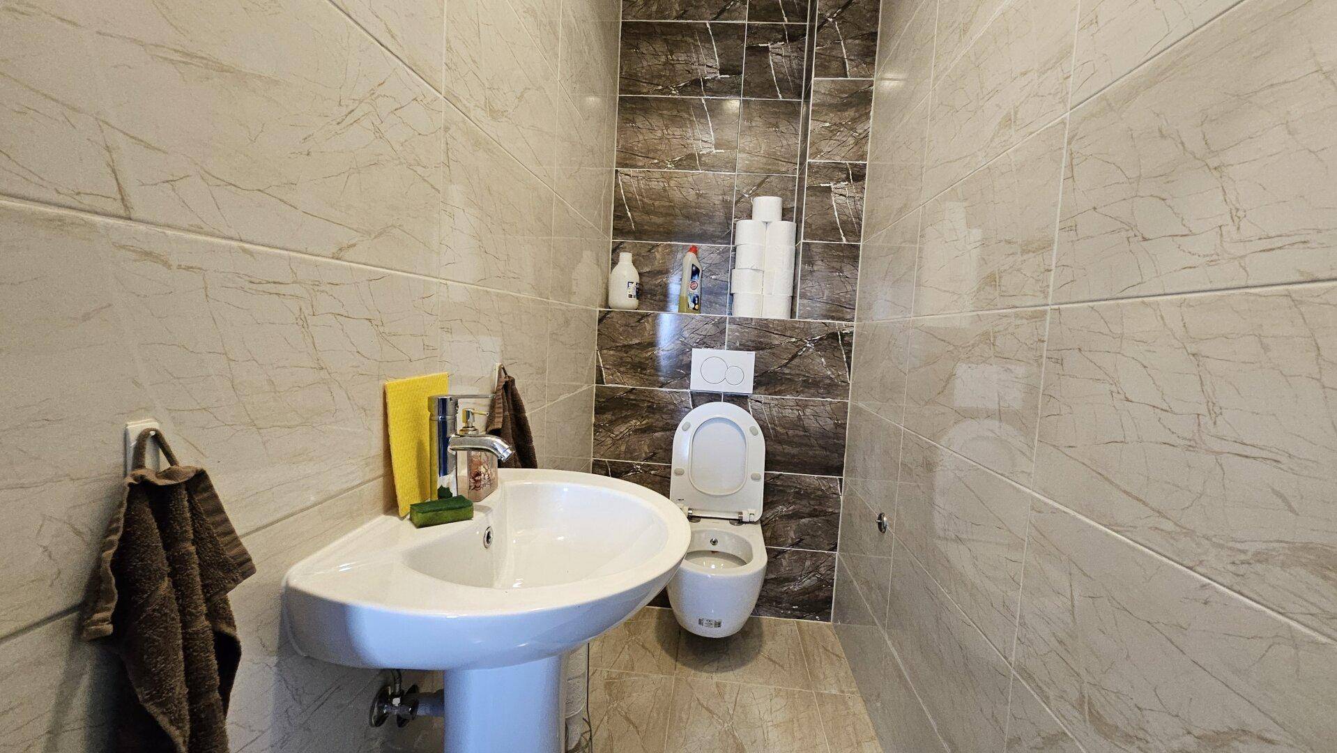 Kleines Badezimmer mit modern gefliesten Wänden, einem Standwaschbecken und einer Toilette.