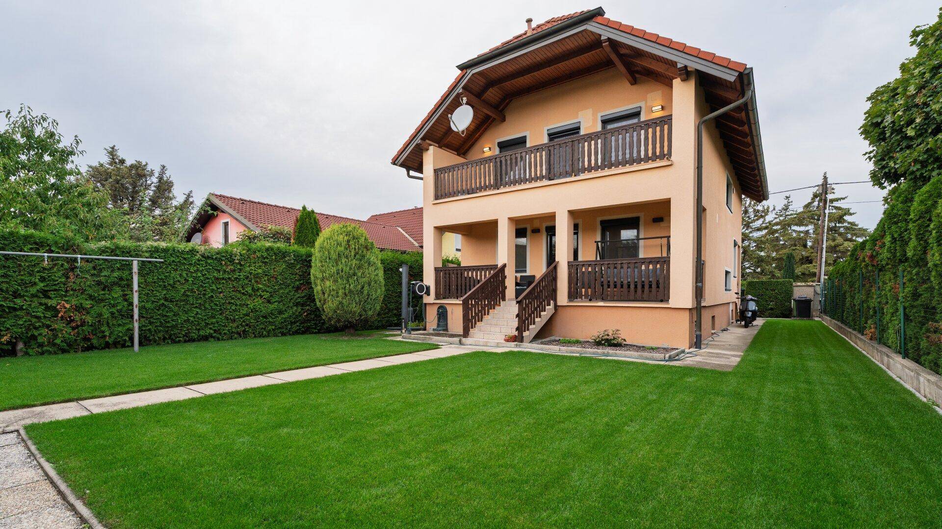 Seitliche Ansicht des Einfamilienhauses mit großem, gepflegtem Rasen und grüner Hecke.