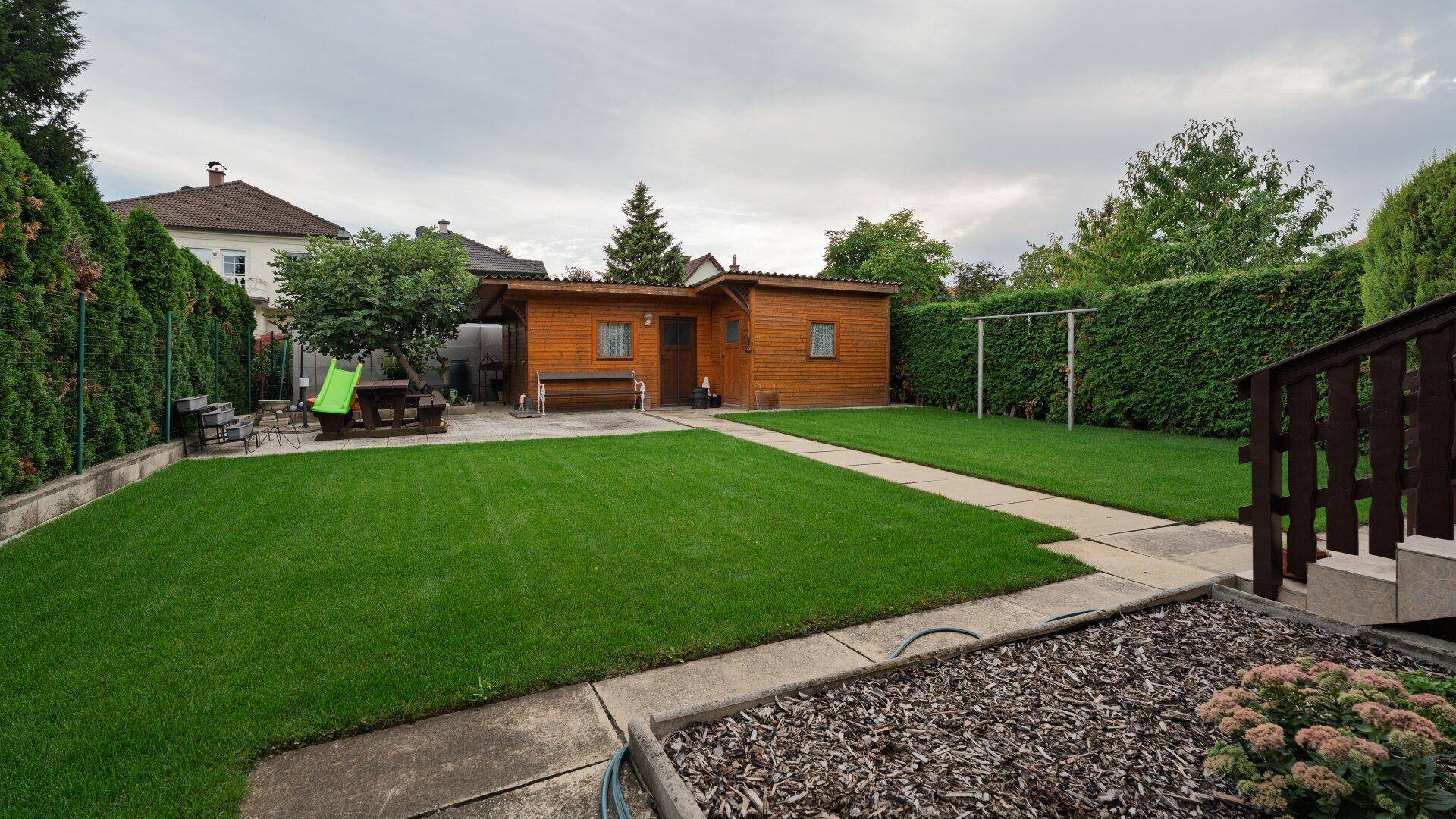 Großer, gepflegter Garten mit Rasenfläche, Gartenhaus und einem Bereich für Outdoor-Aktivitäten.