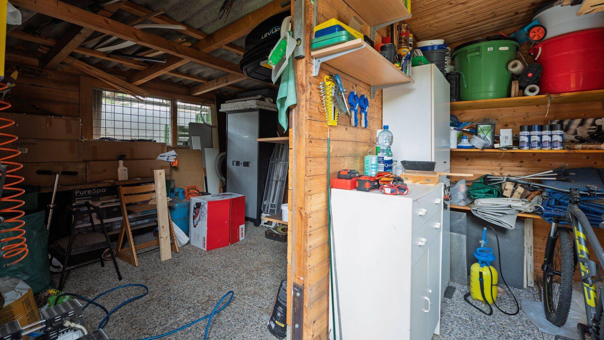 Weiterer Blick in das Gartenhaus mit vielen Regalen, Werkzeugen und gelagerten Gegenständen.