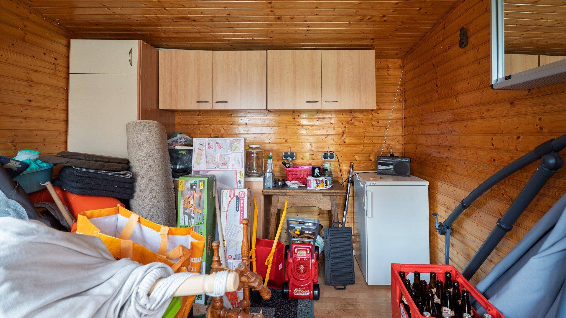 Innenansicht des Gartenhauses mit Holzverkleidung, Regalen und verschiedenen gelagerten Gegenständen.