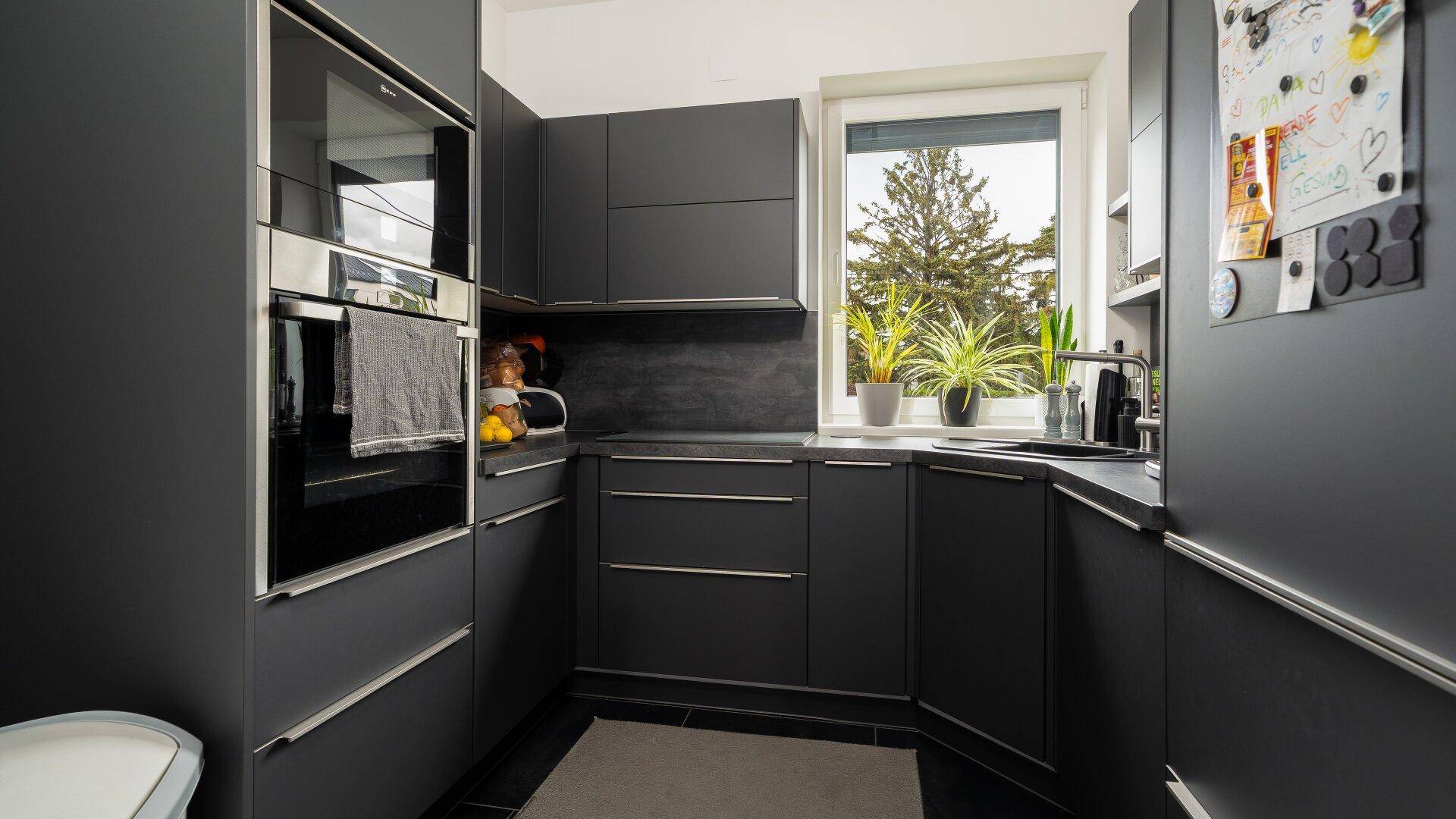 Moderne schwarze Küche mit Einbaugeräten, Fenster und Pflanzen auf der Fensterbank.